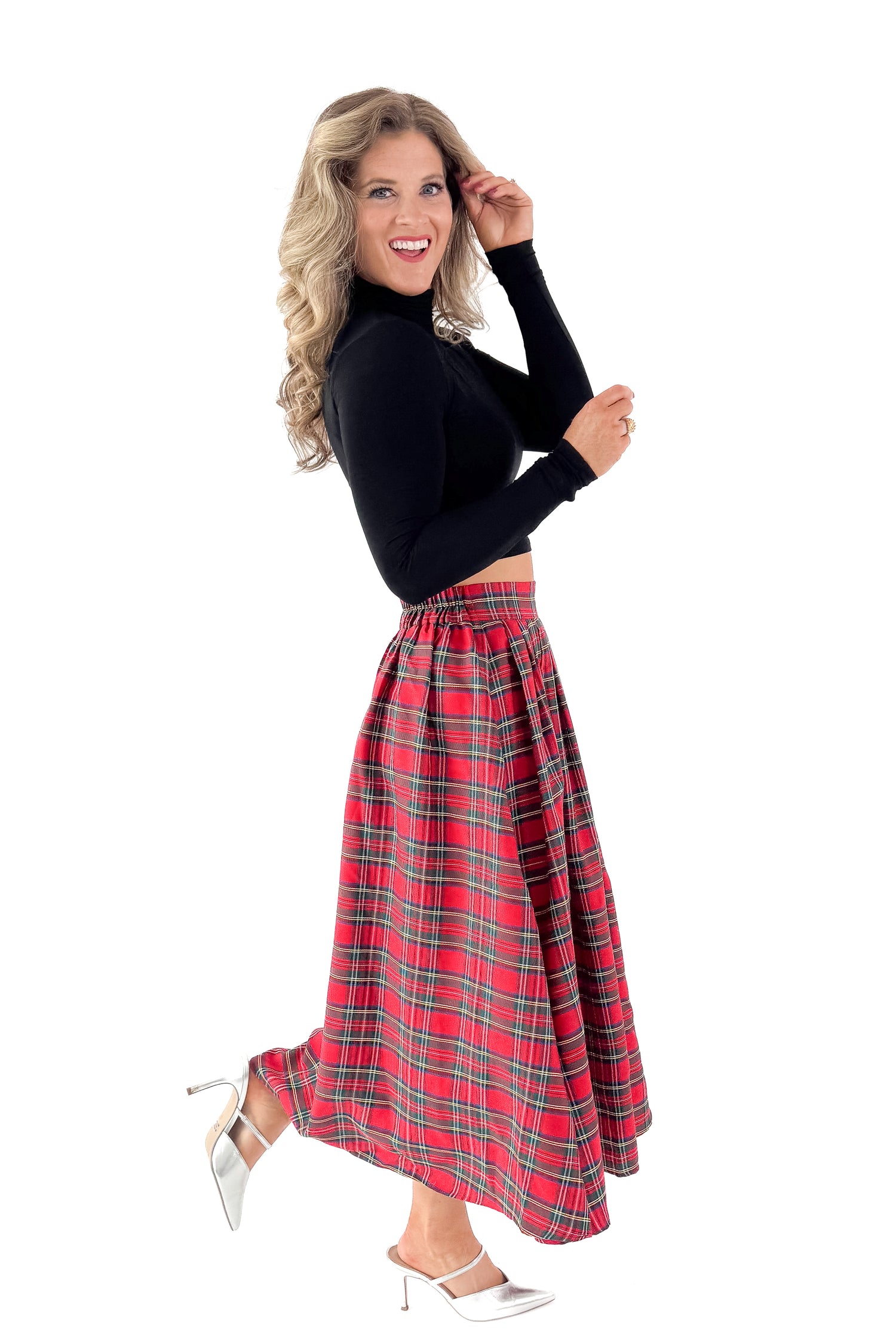 Side view of woman wearing black top with red tartan skirt against white studio background.