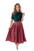 Front view of woman wearing green sweater with red tartan skirt against white studio background.