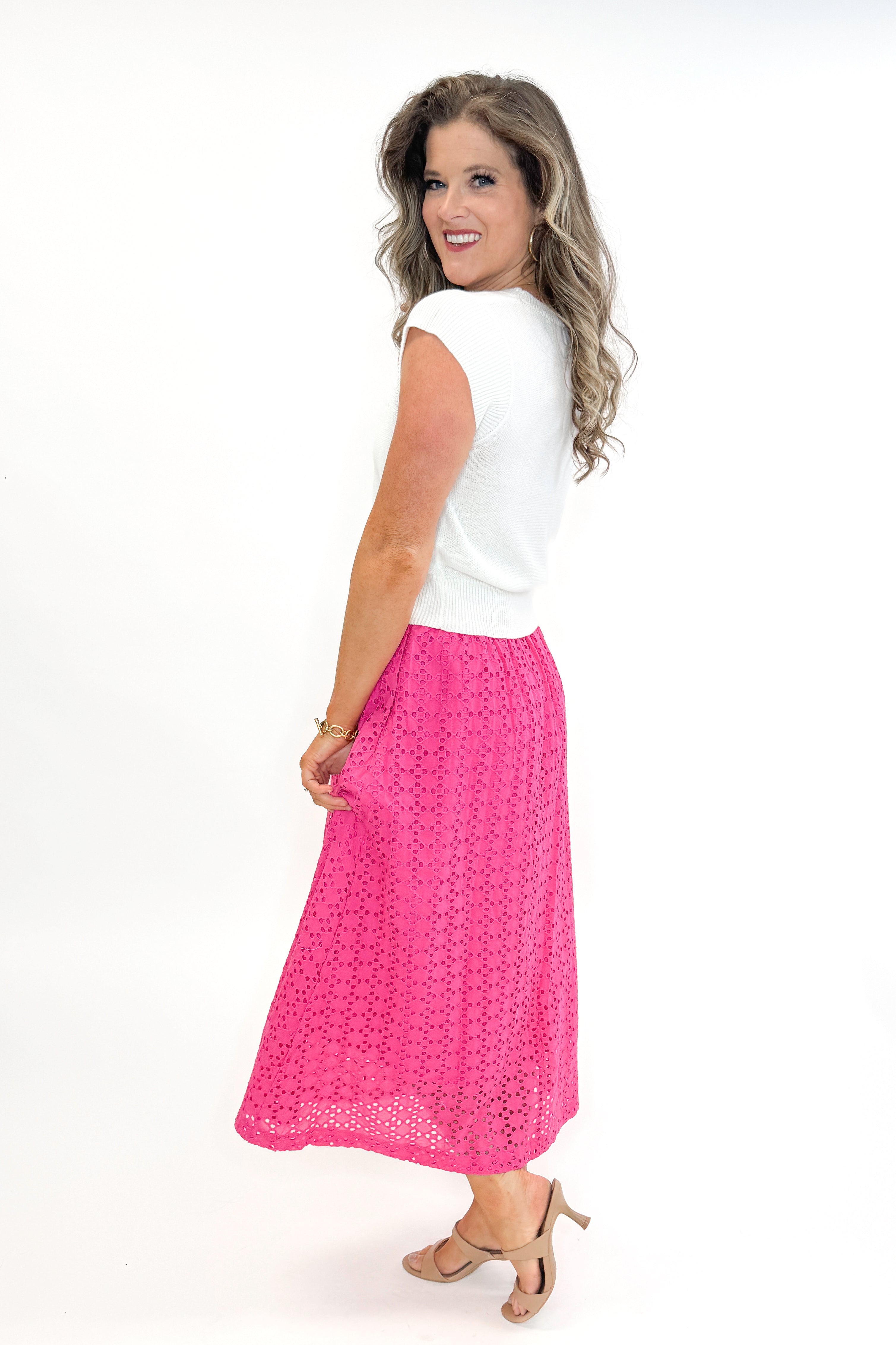 Side view of woman wearing white sweater with Hot Pink Eyelet Midi Skirt by Entro against white studio background.