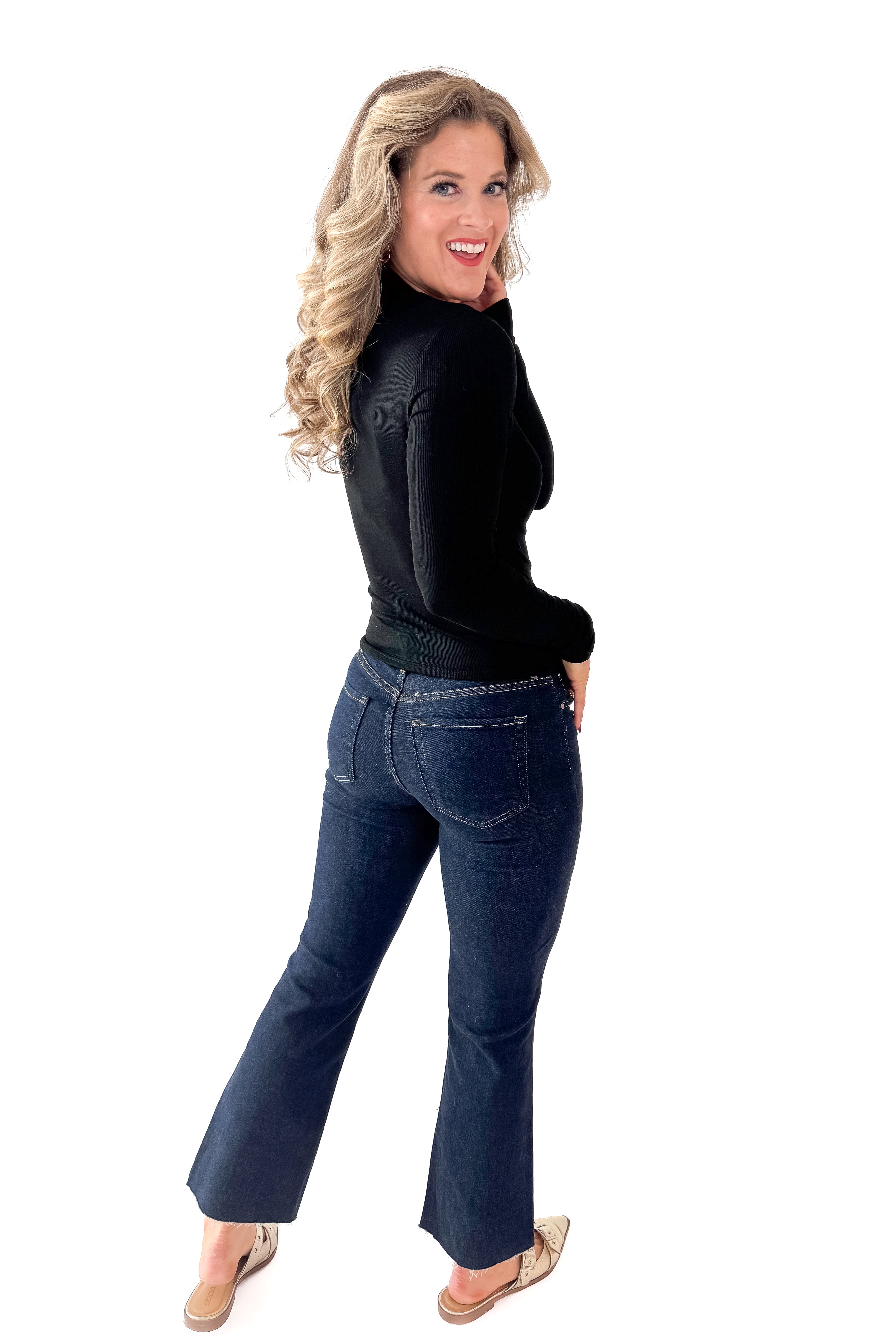 Side view of woman wearing Black Ribbed Mock Neck Top with jeans against white studio background.