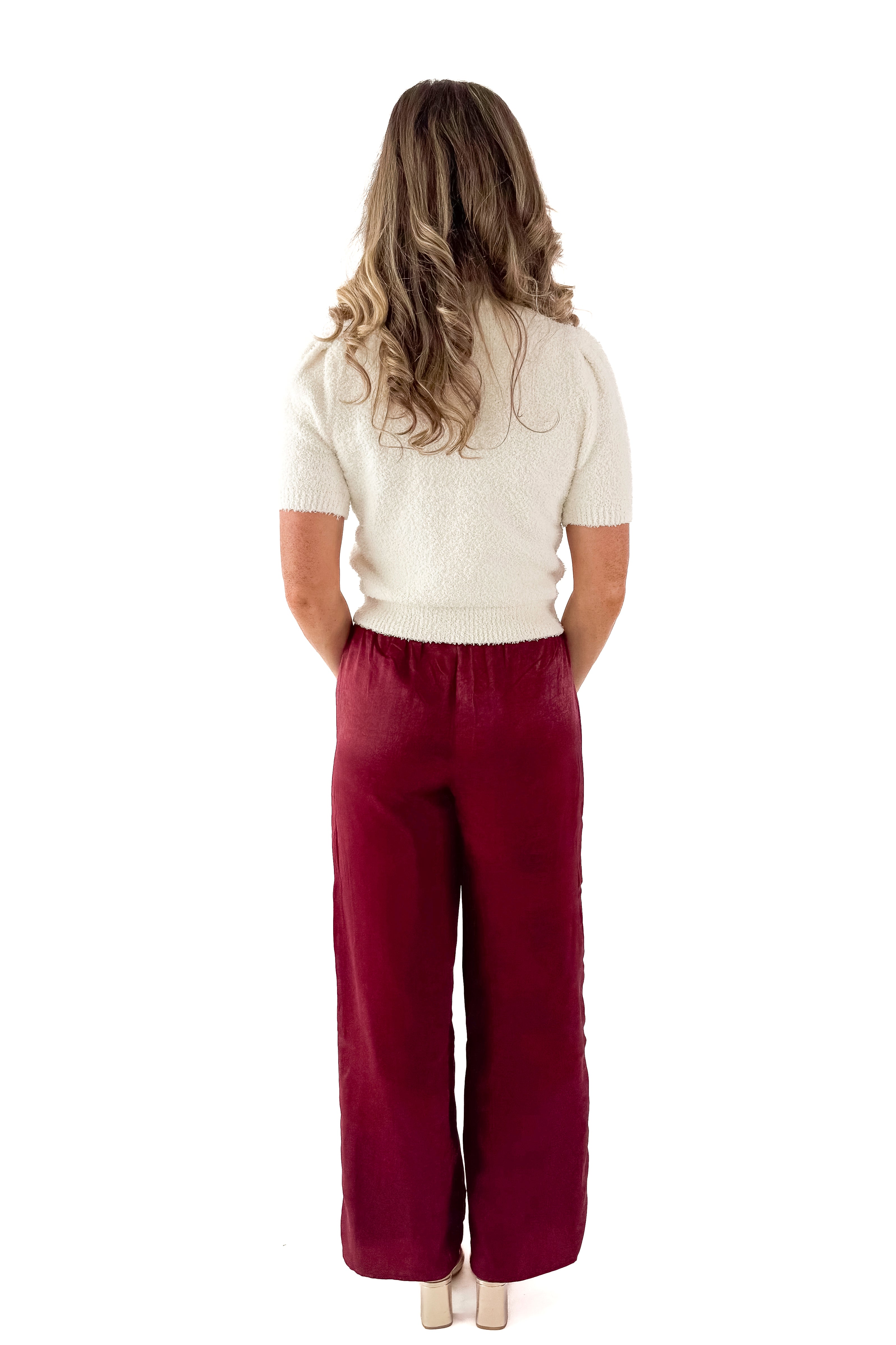 Back view of woman wearing cream sweater and Wine Satin Wide Leg Pants against white studio background.