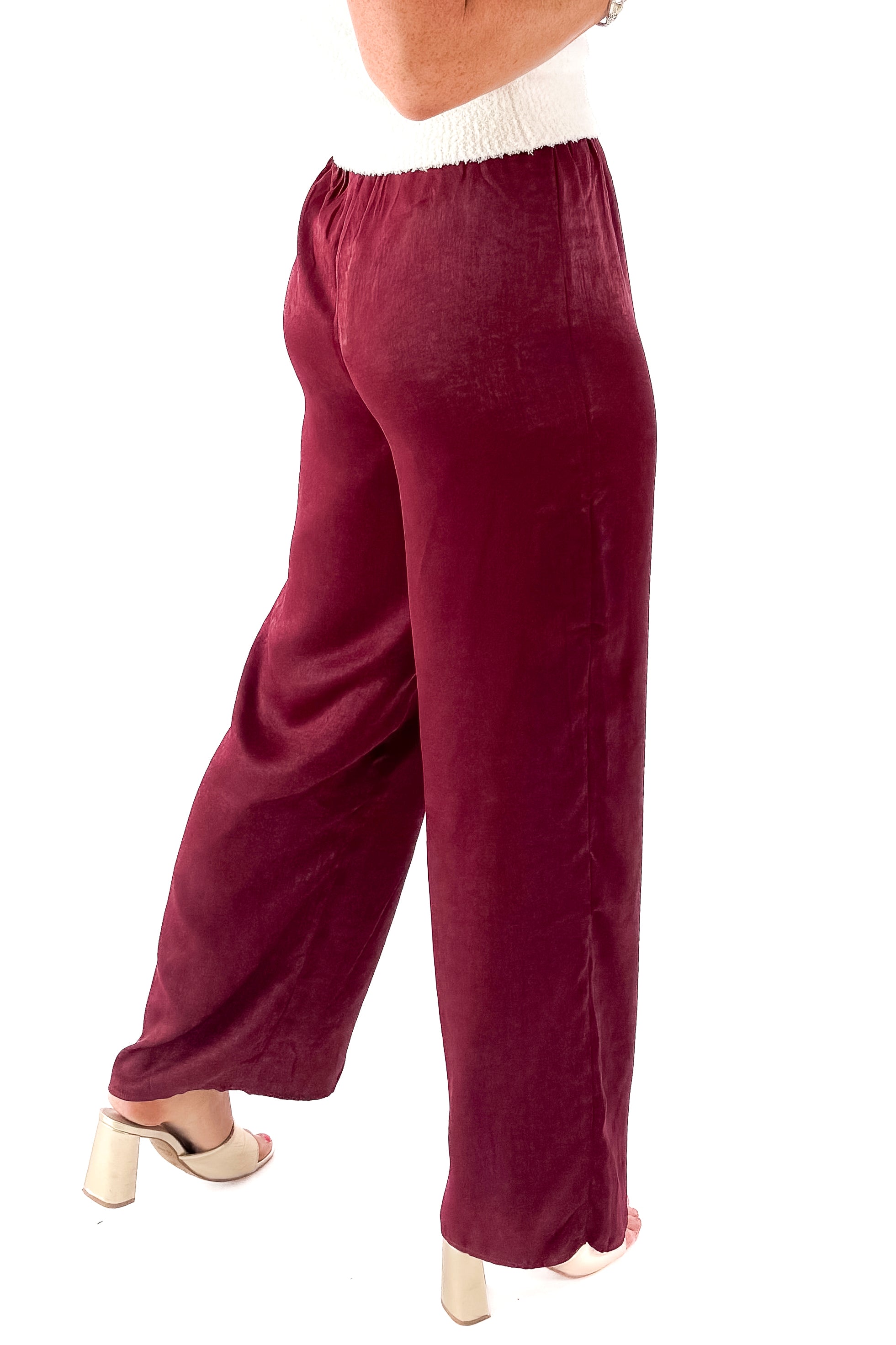 Side view of woman wearing cream sweater and Wine Satin Wide Leg Pants against white studio background.