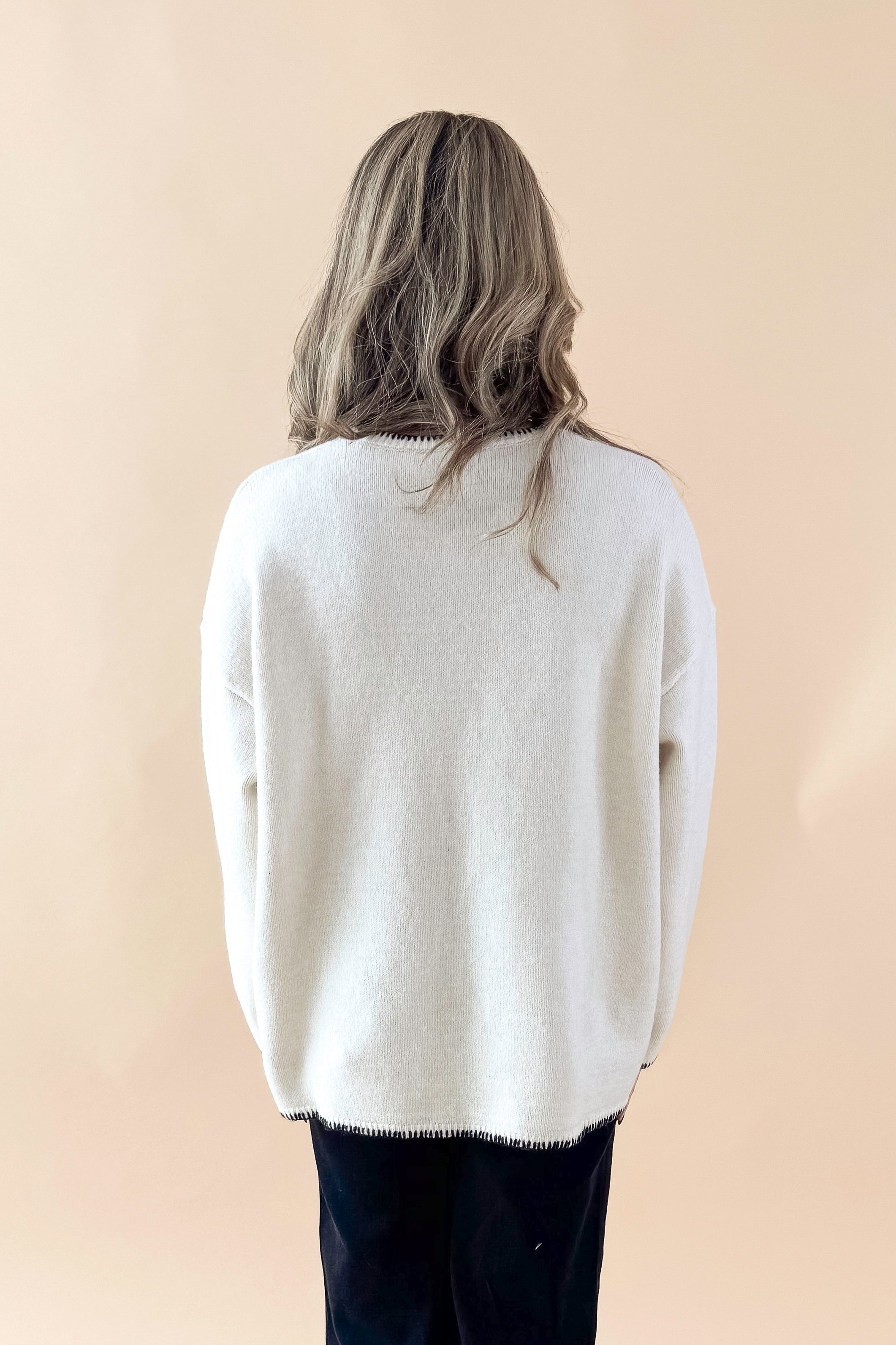 Back view of woman wearing Cream Pocket & Stitch Detail Sweater with jeans against tan studio background.