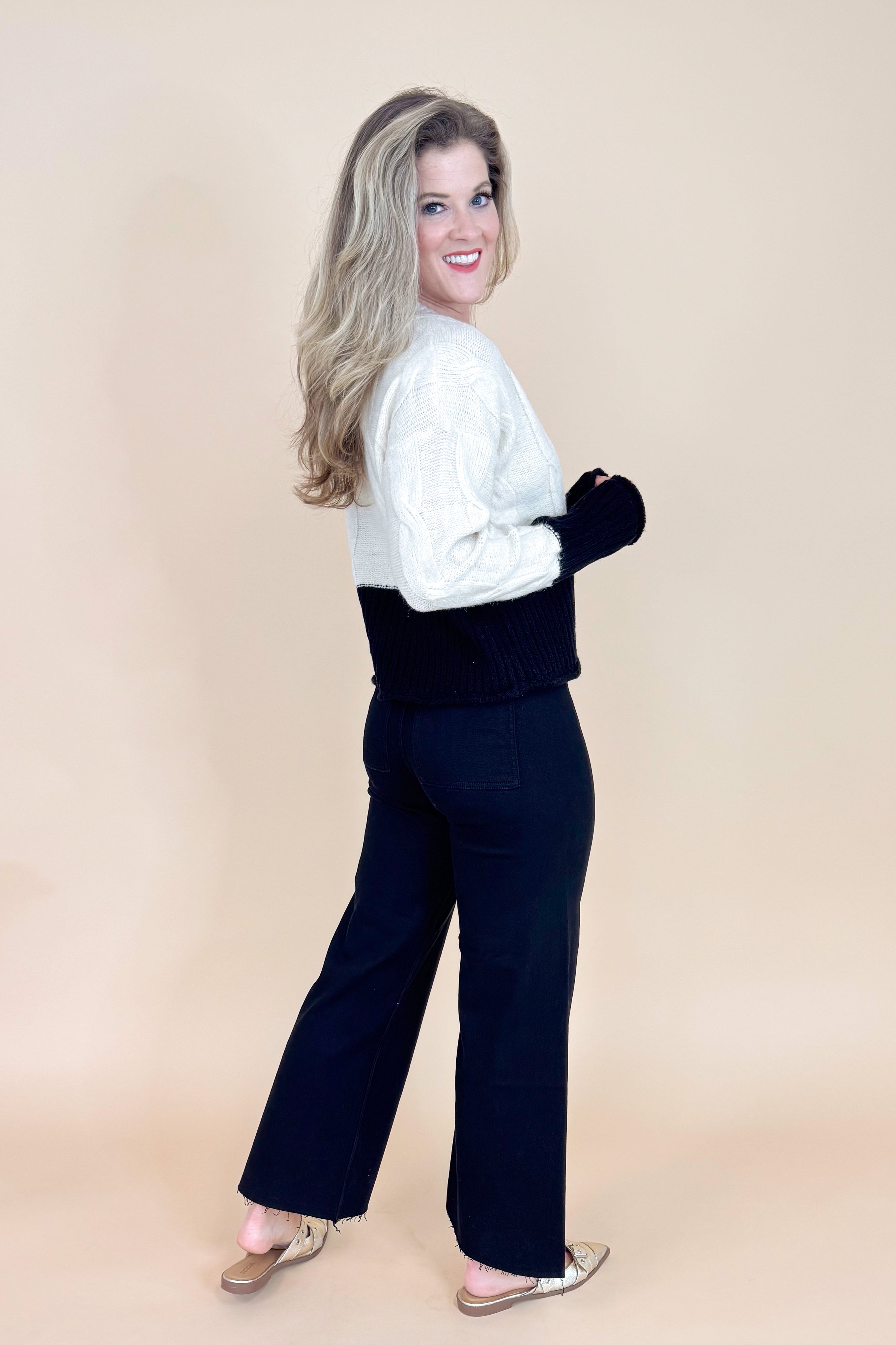 Woman wearing a white sweater and black pants on a beige background