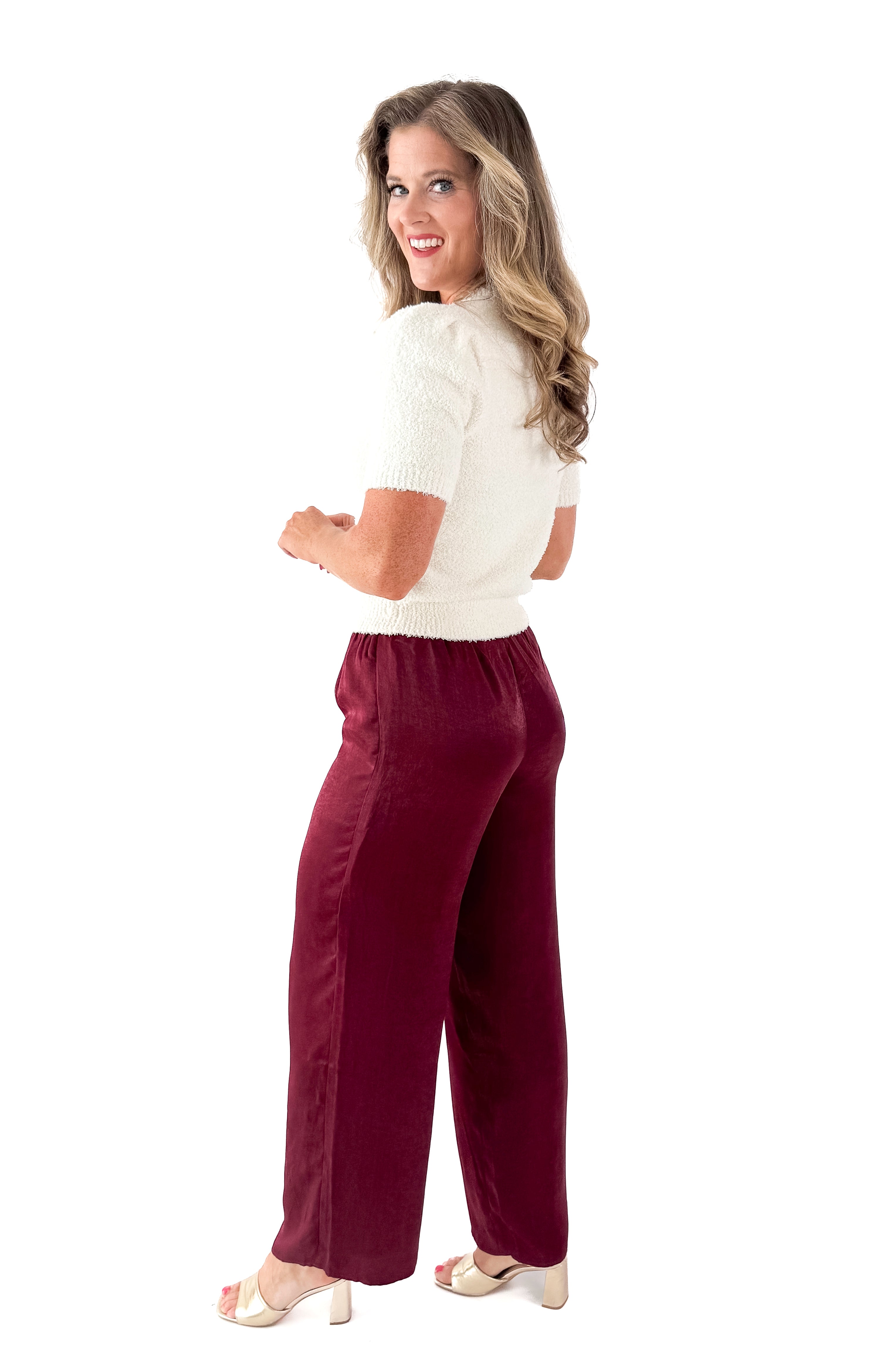 Side view of woman wearing Cream Fuzzy Short Sleeve Sweater with burgundy pants against white studio background.