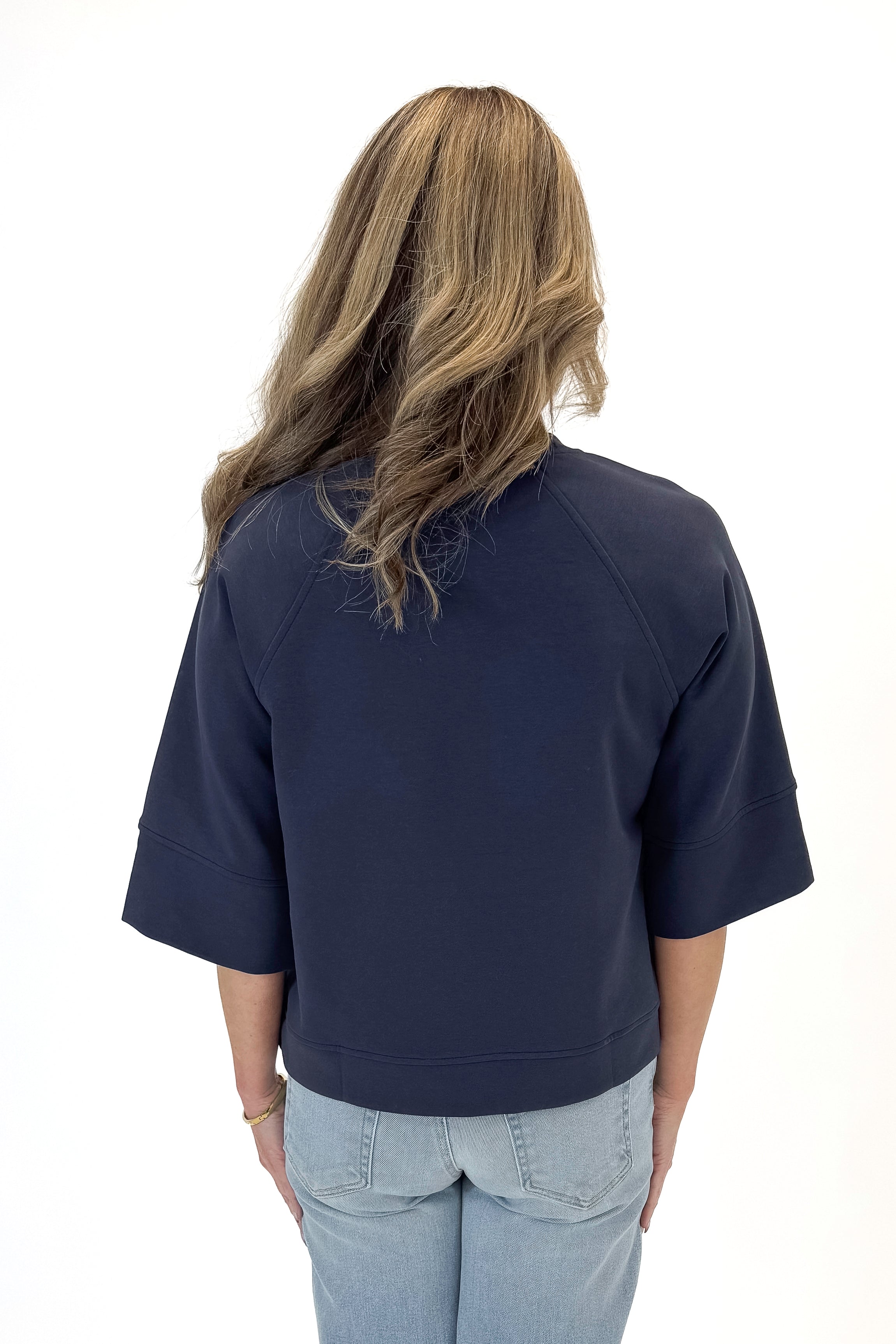 Back view of woman wearing Navy Super Soft Half Sleeve Top with jeans against white studio background.