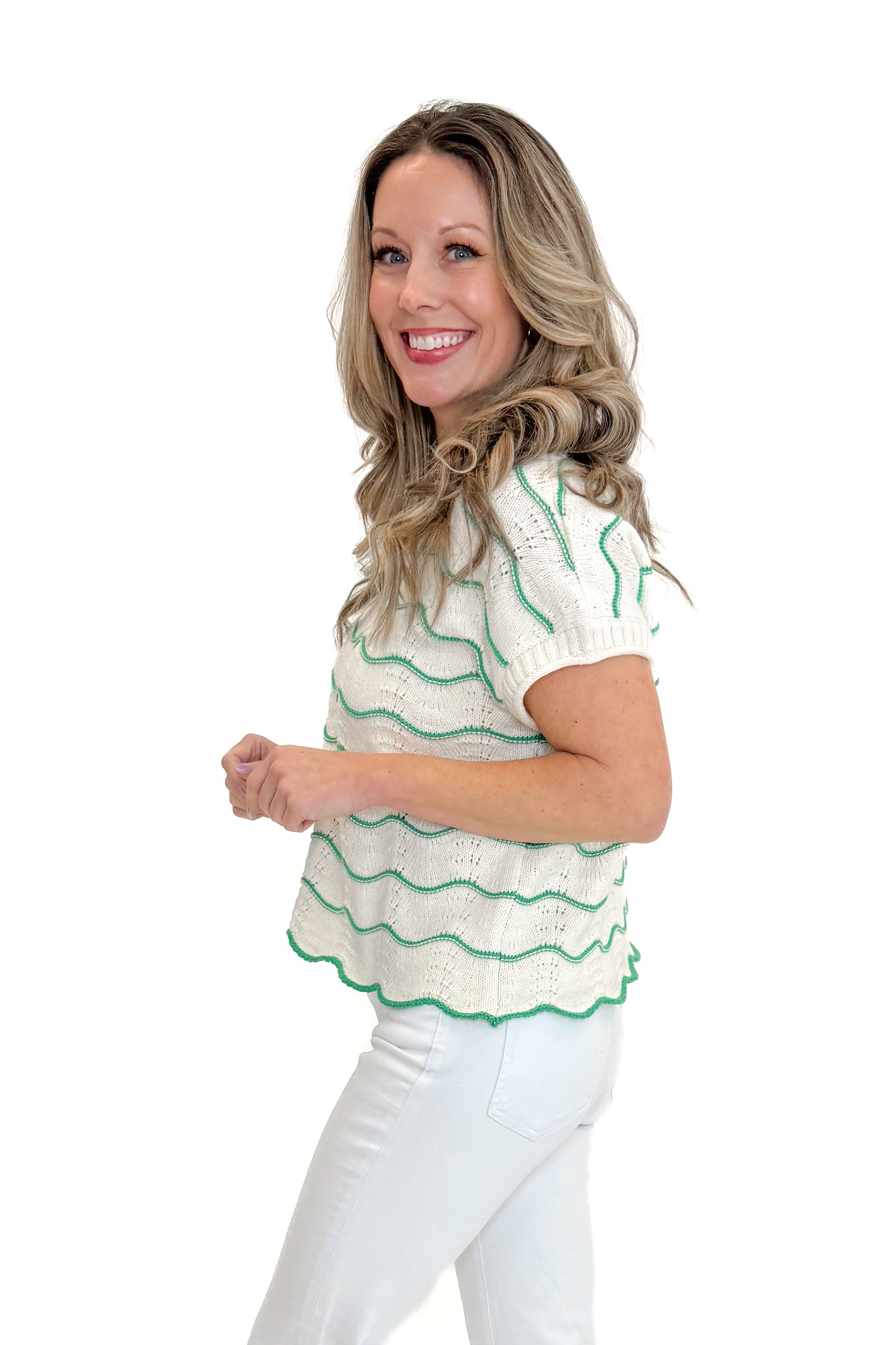 Side view of woman wearing Green & Cream Scallop Detail Short Sleeve Sweater with jeans against white studio background.