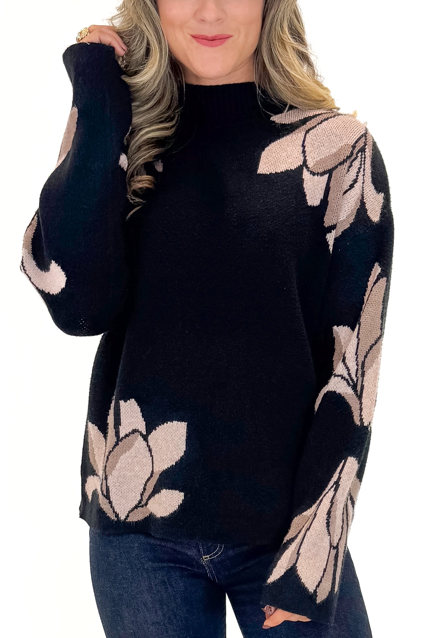 Front detail view of woman wearing Black With Mauve Floral Print Sweater with jeans against white studio background.
