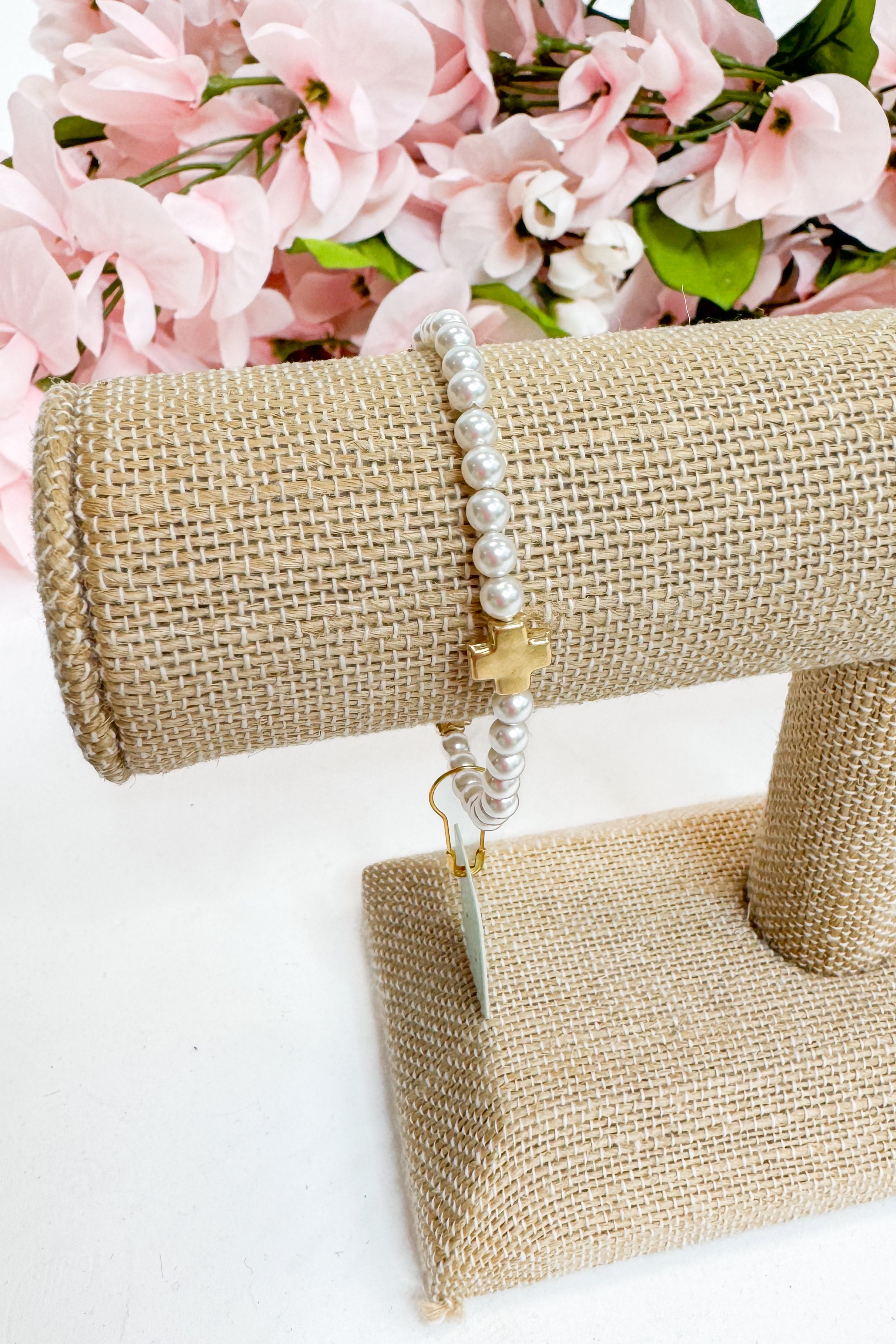 Pearl bracelet on a burlap stand with pink flowers in the background