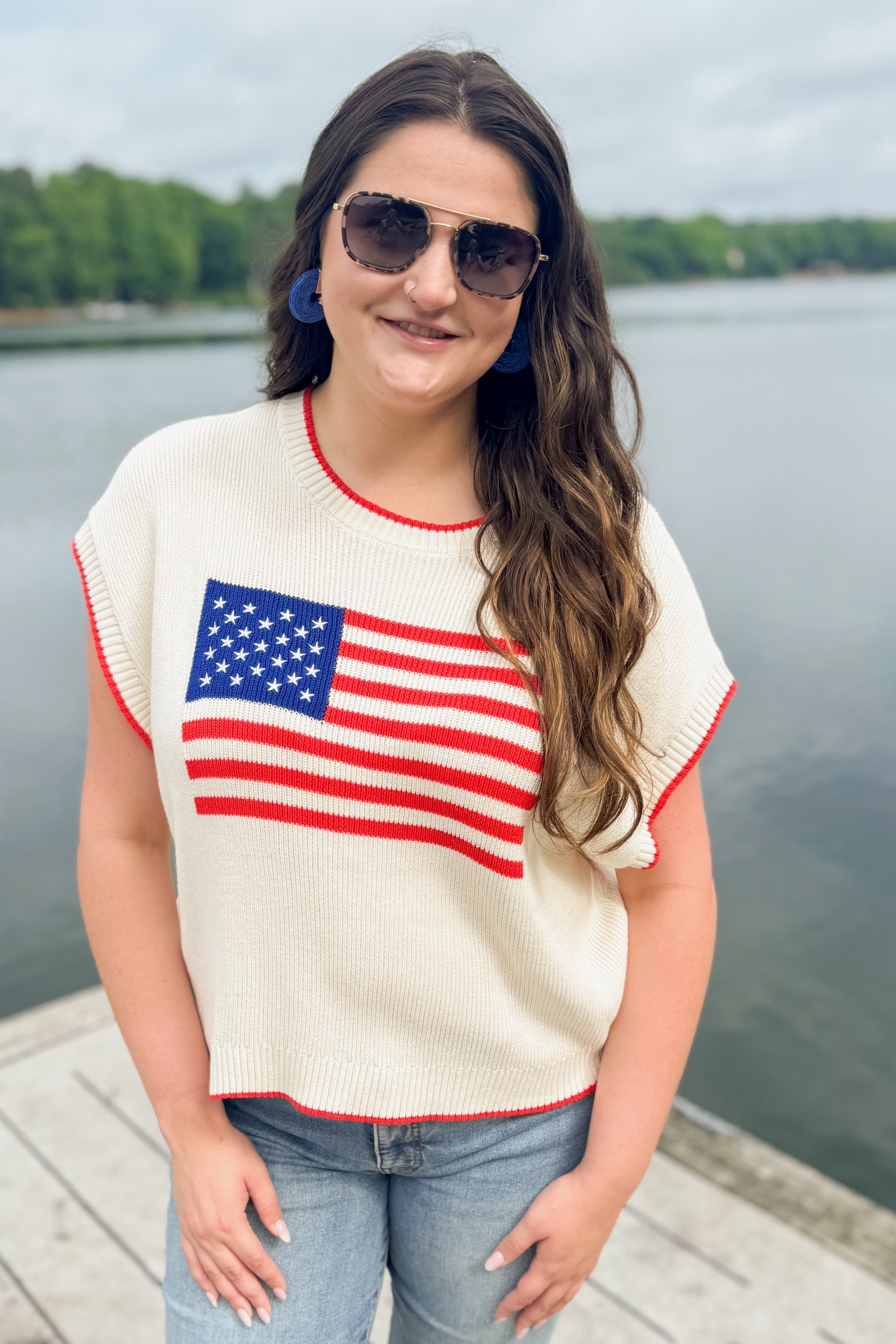 Front view of woman wearing Swagger Boutiqueās Sleeveless Patriot Sweater In Cloud by Z Supply with jeans stsanding outside at the lake.