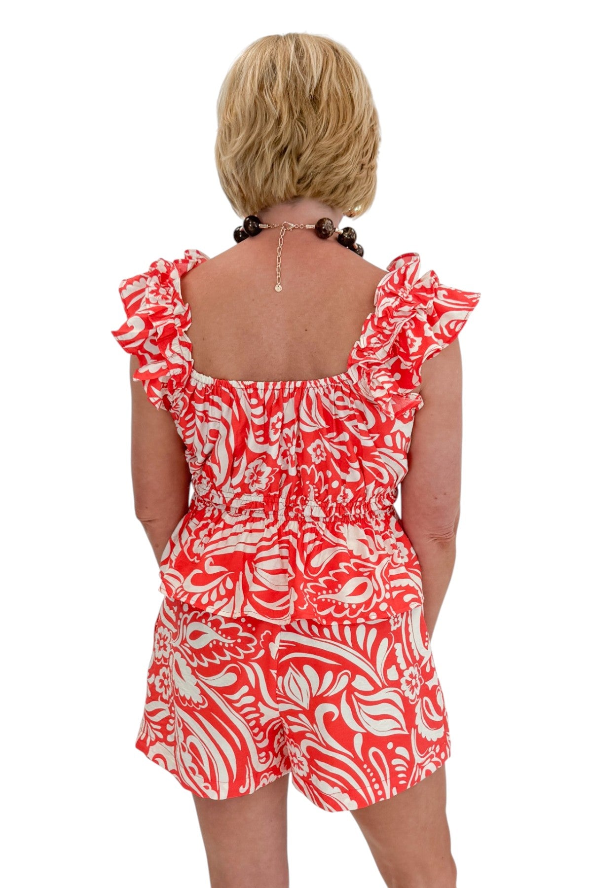 Back view of woman wearing Swagger Boutiqueās Coral Printed Smocked Peplum Tank with matching Coral Printed Shorts against white studio background.