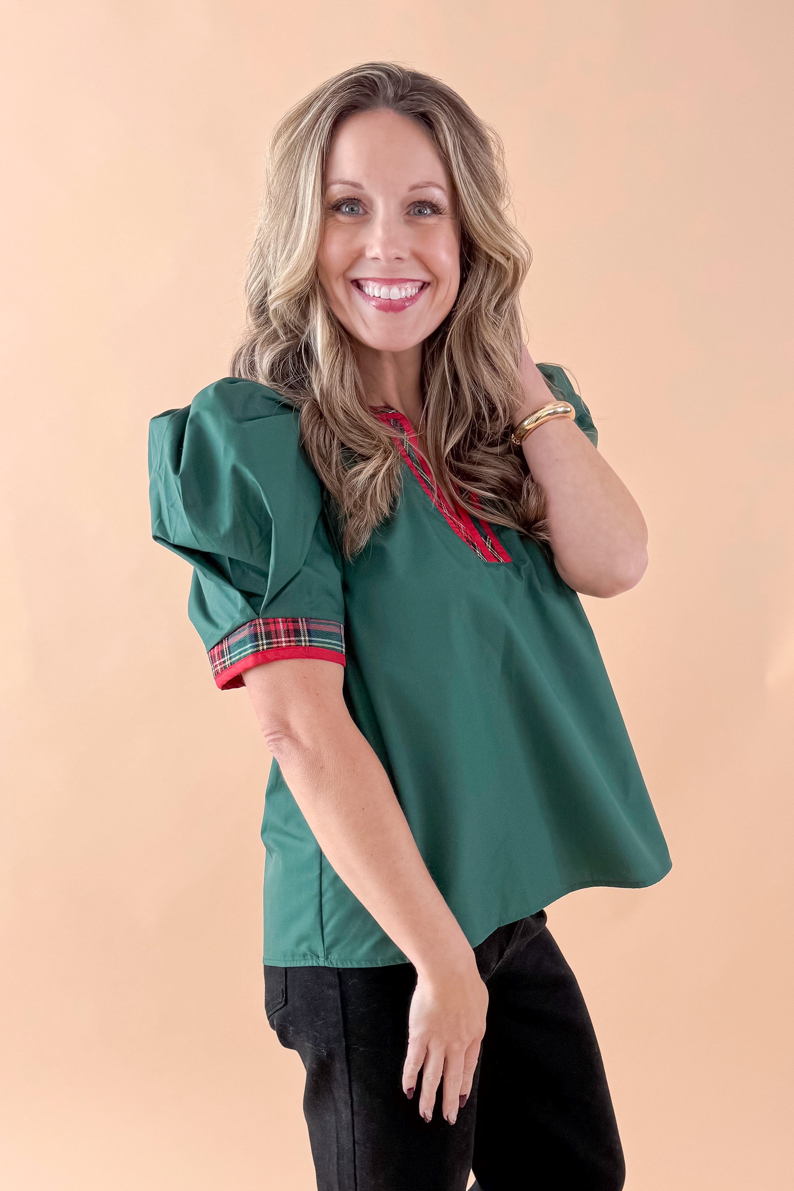 Side view of woman wearing Green With Tartan Lining Puff Sleeve Top with jeans against tan studio background.