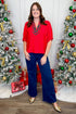 Front view of woman wearing red top with blue jeans with Christmas trees in the background.