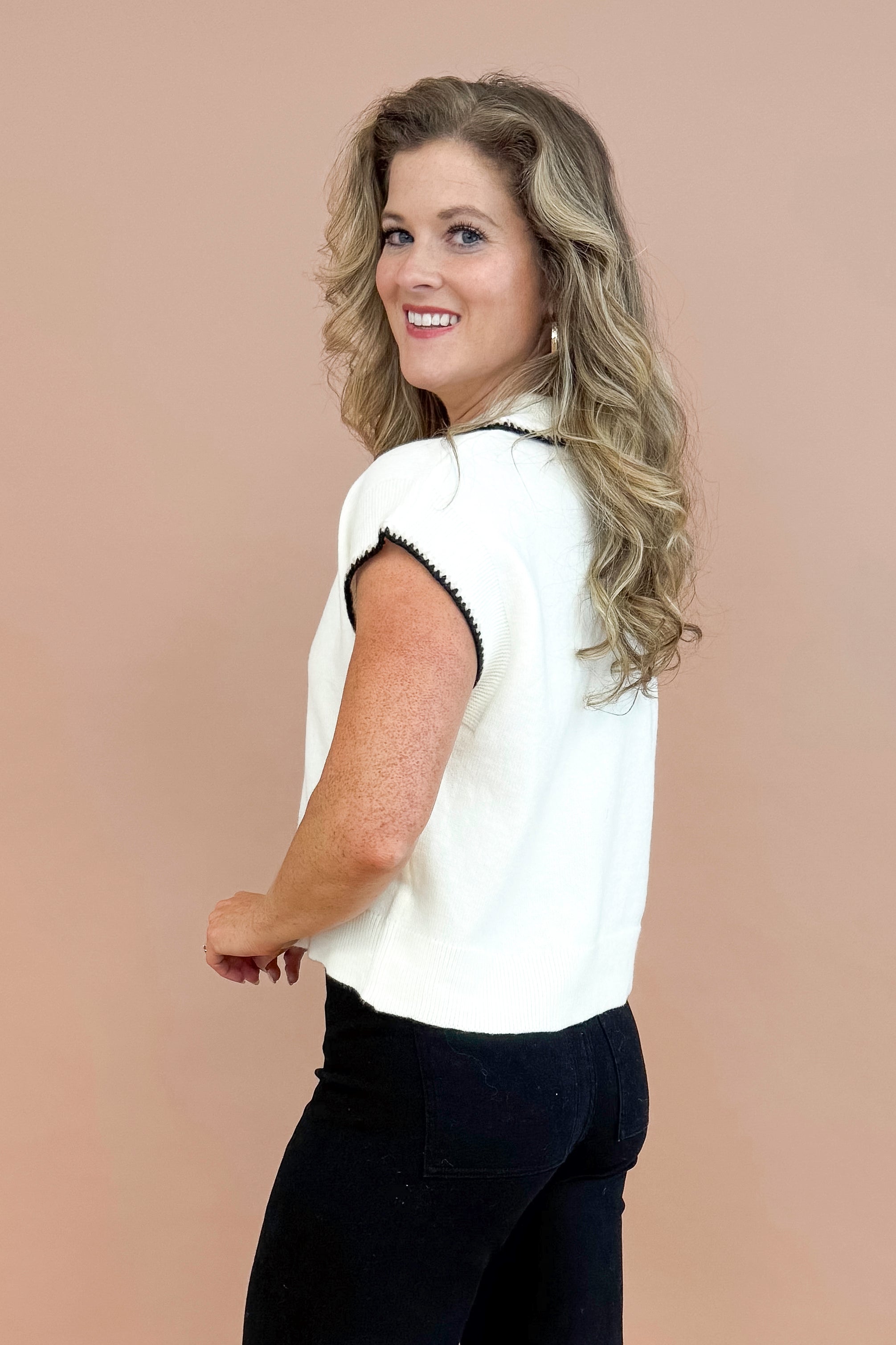 Side view picture of woman wearing Cream With Black Stitching Short Sleeve Sweater by Entro and jeans with taupe background.
