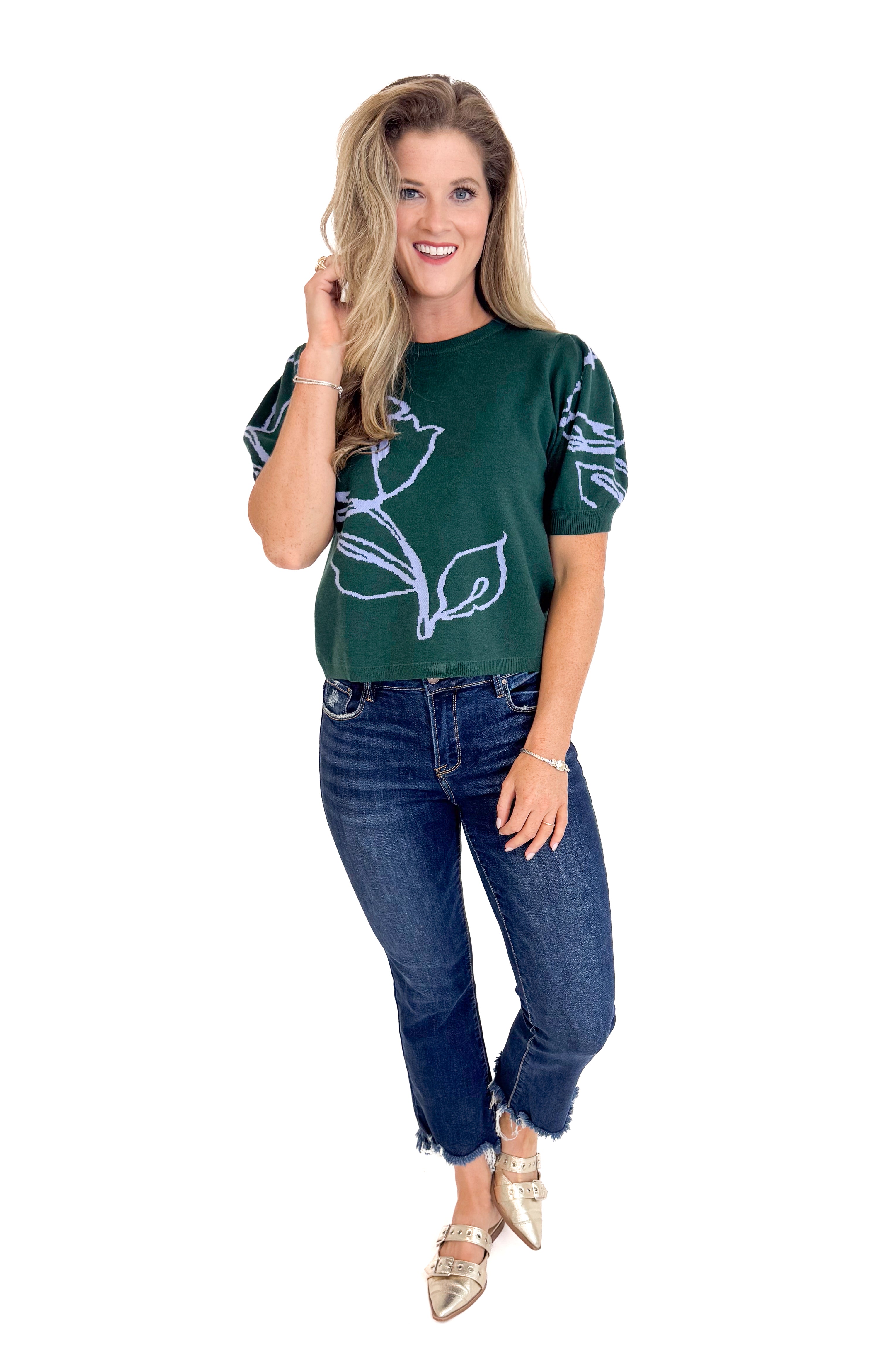 Woman wearing a dark green t-shirt with a floral design and blue jeans on a white background