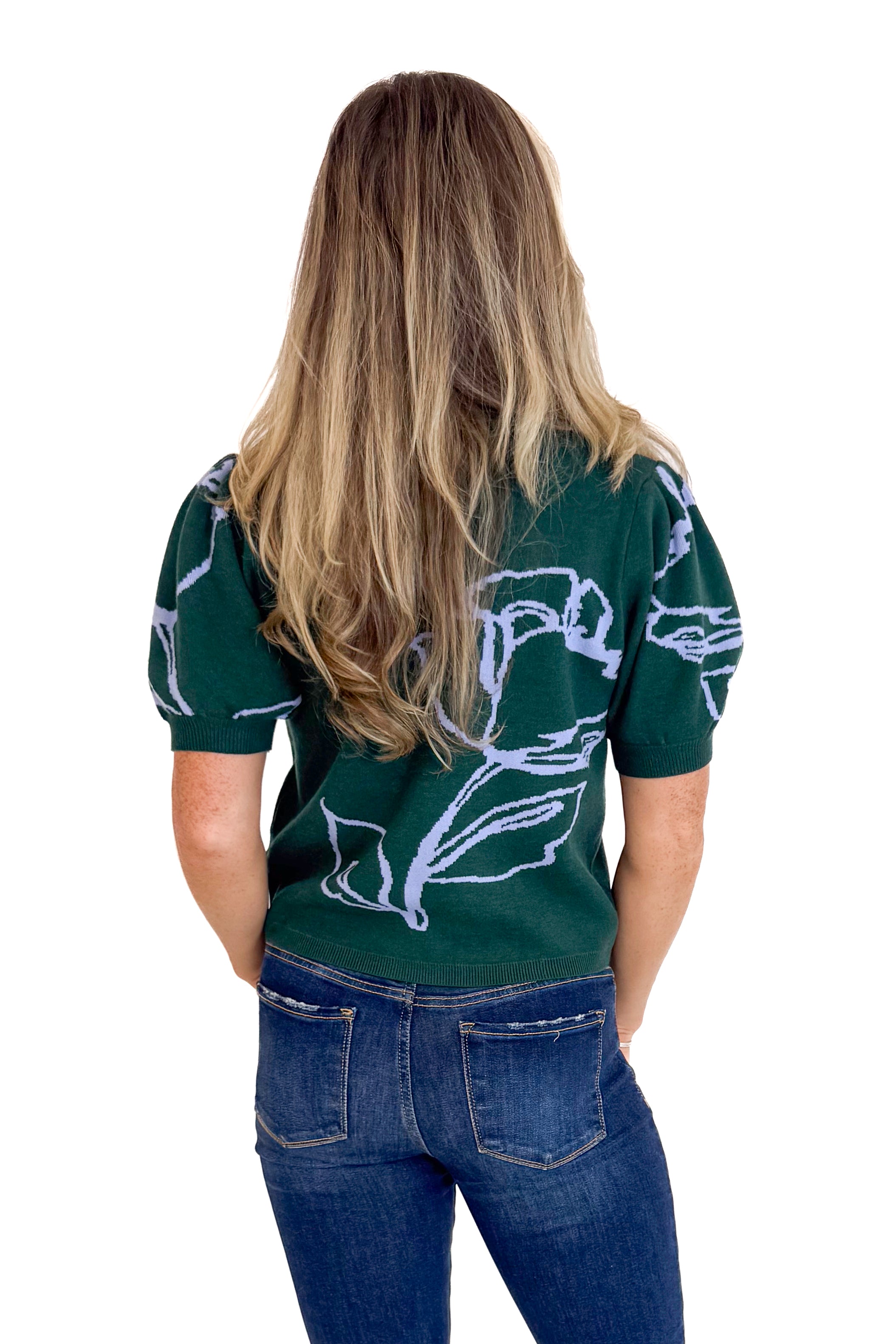 Person wearing a dark green shirt with floral patterns on the back, standing against a white background.