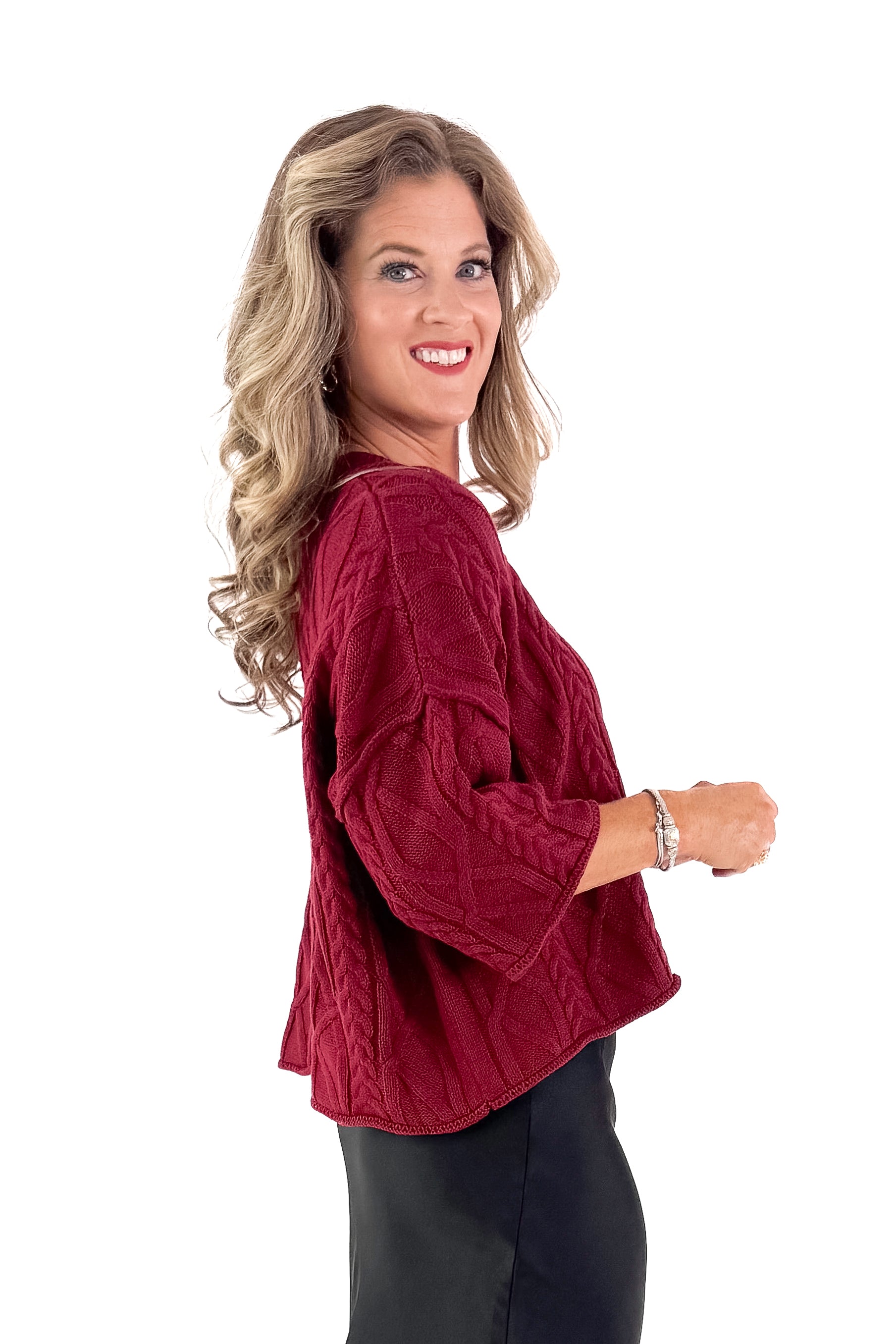 Side view of woman wearing Burgundy Cable Knit 3/4 Sleeve Sweater with black skirt against white studio background.