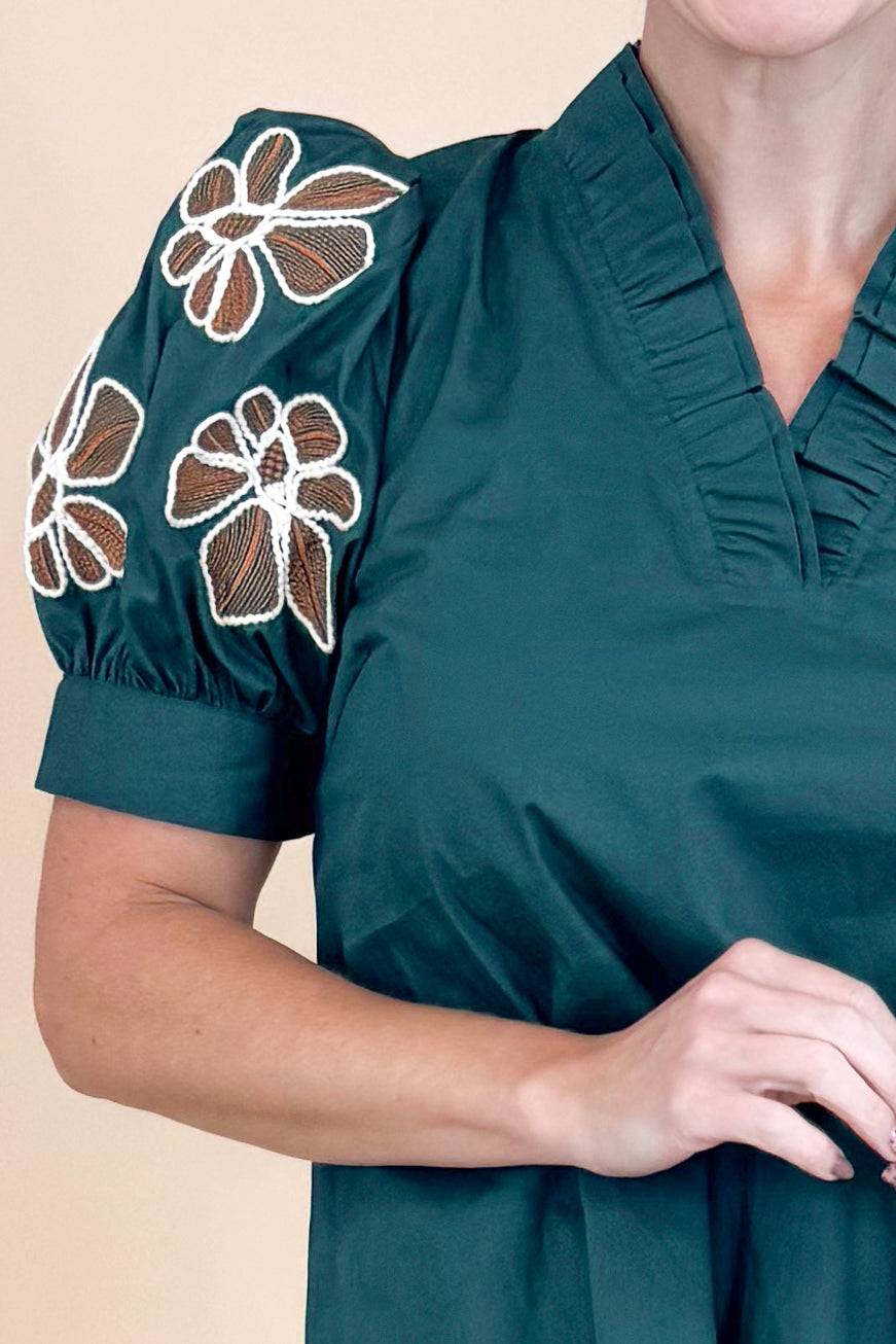 Green blouse with floral embroidery on sleeves against a beige background