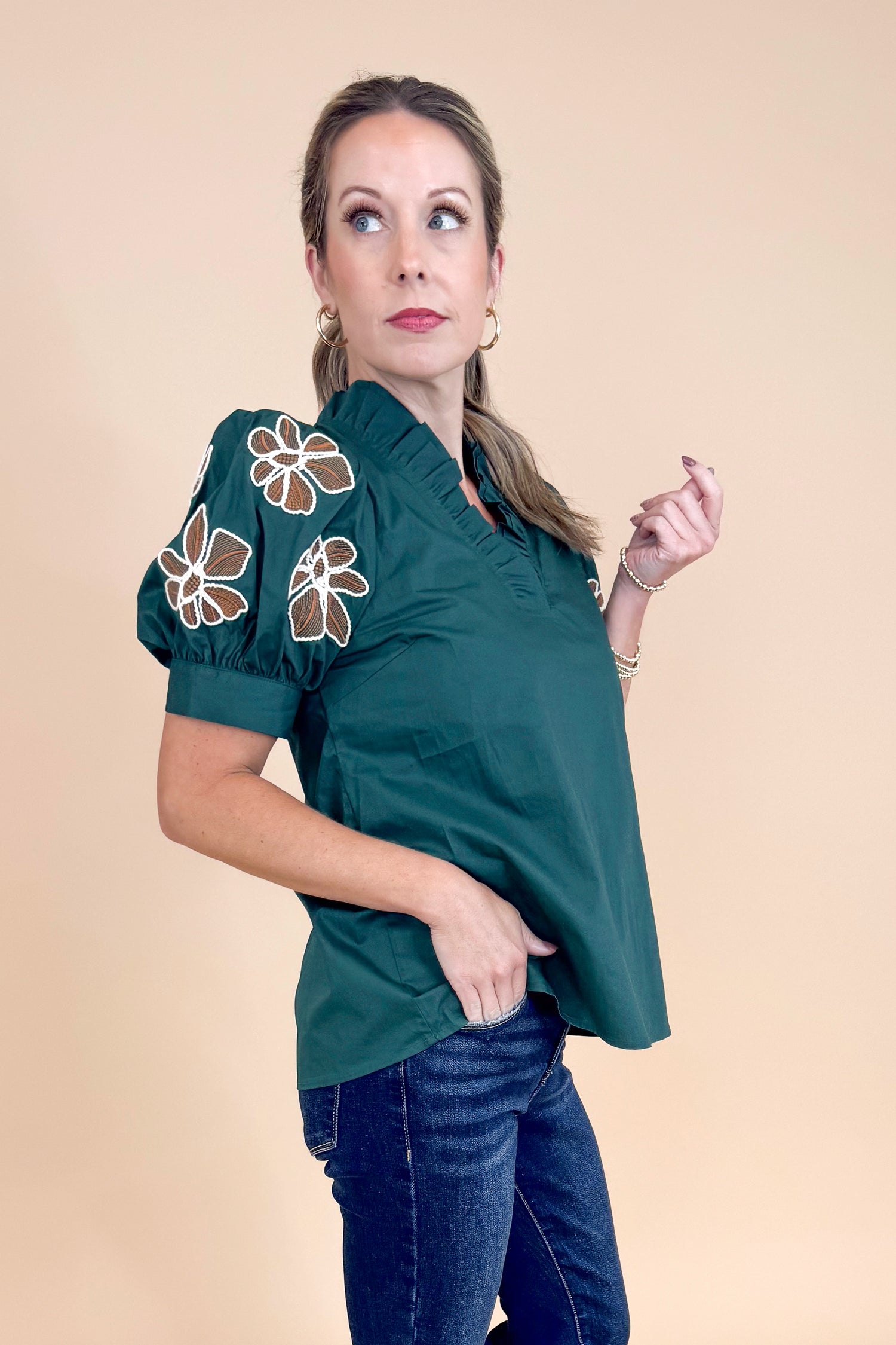 Woman wearing a dark green blouse with floral embroidery on a beige background