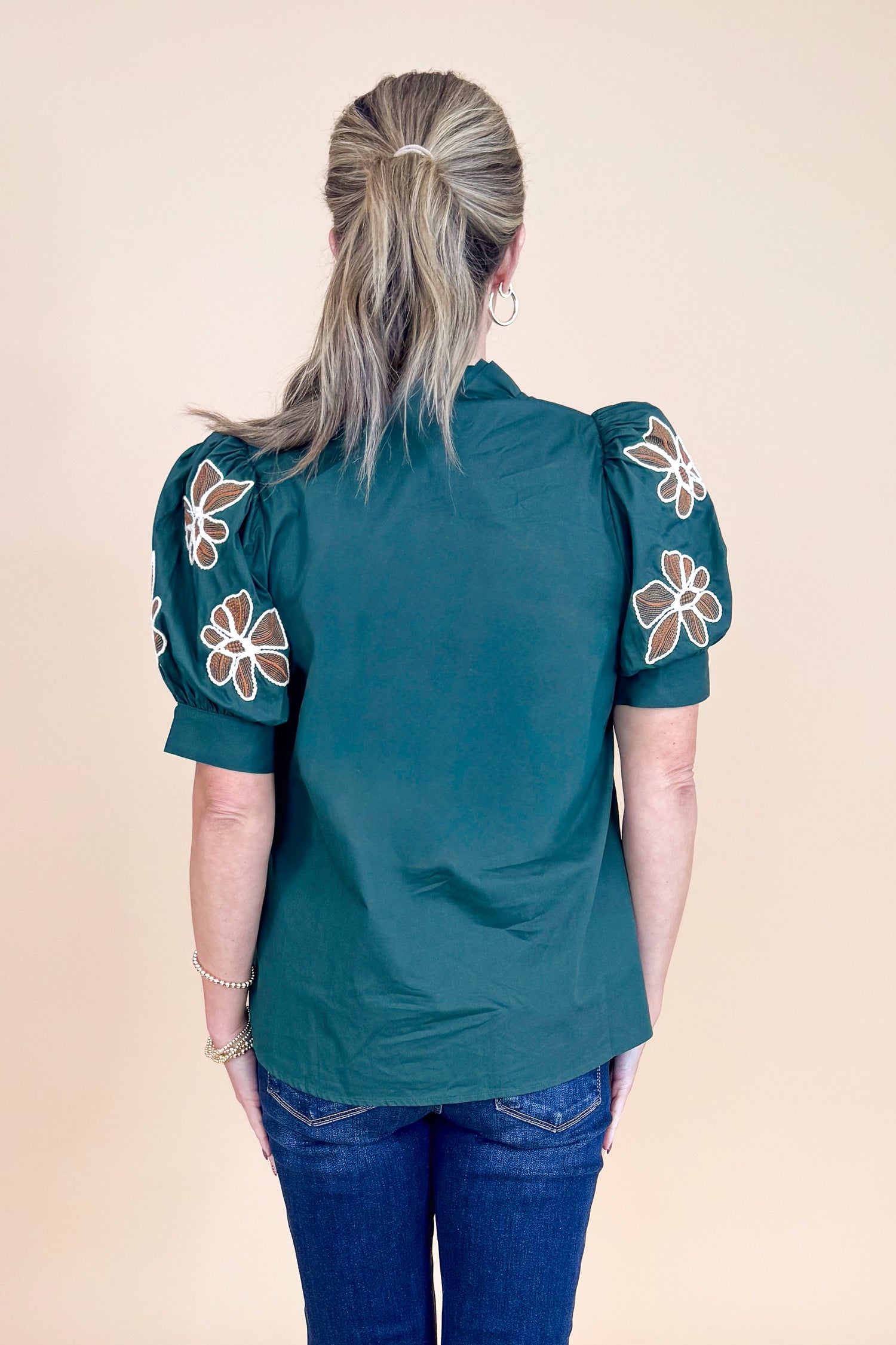 Person wearing a dark green blouse with floral embroidery on a beige background