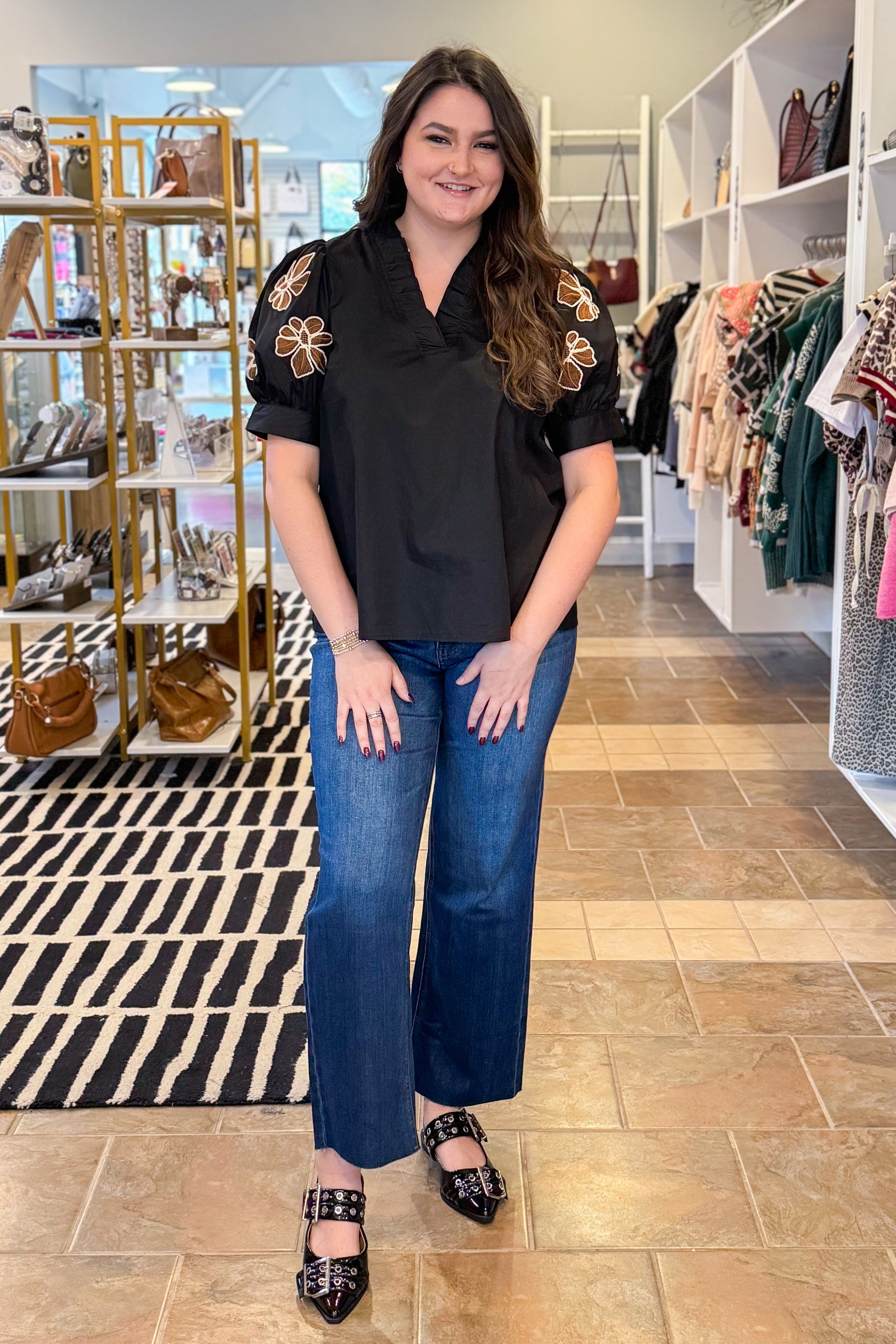Woman in a black top with floral embellishments and blue jeans standing in a store.