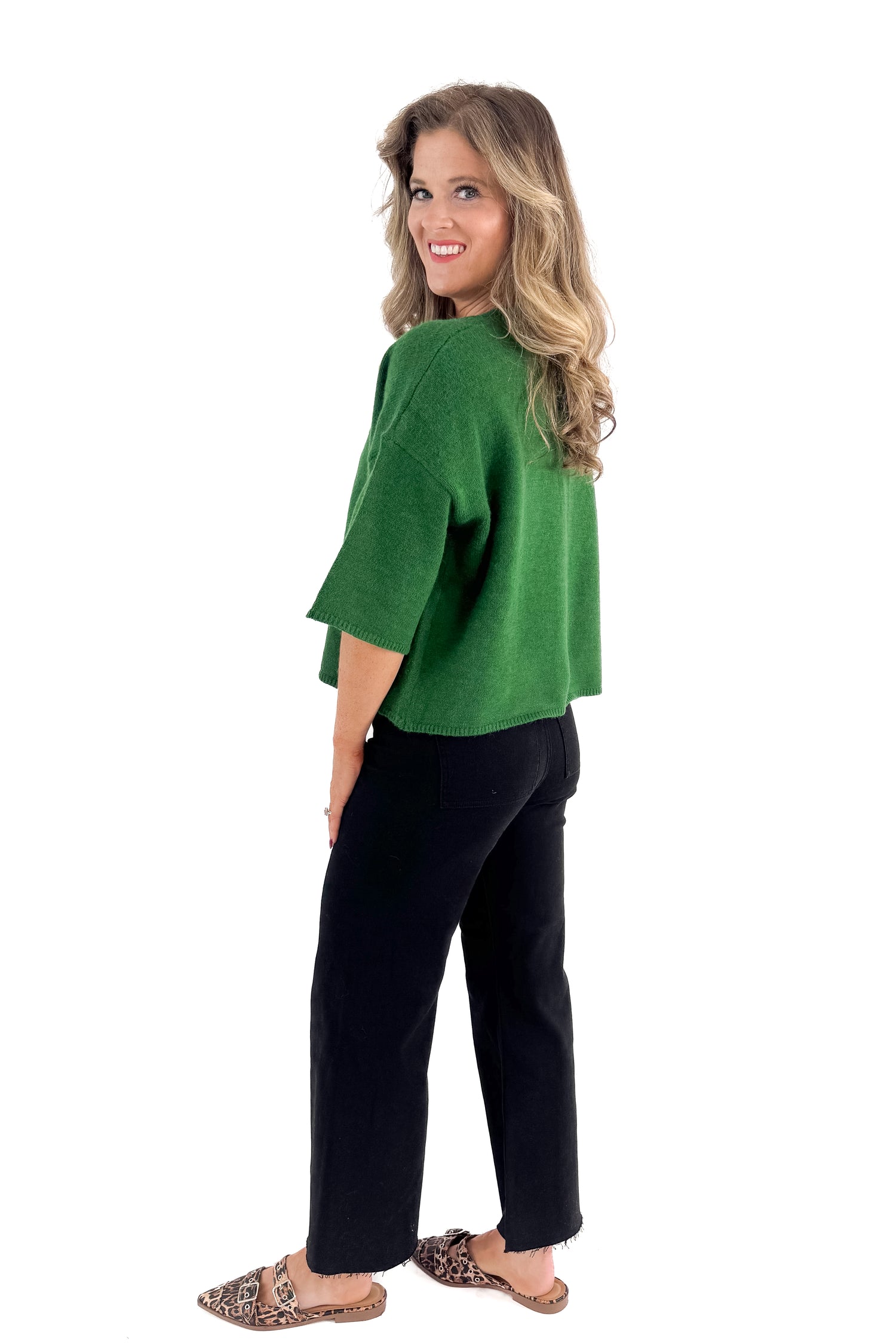 Side view of woman wearing green sweater with jeans against white studio background.