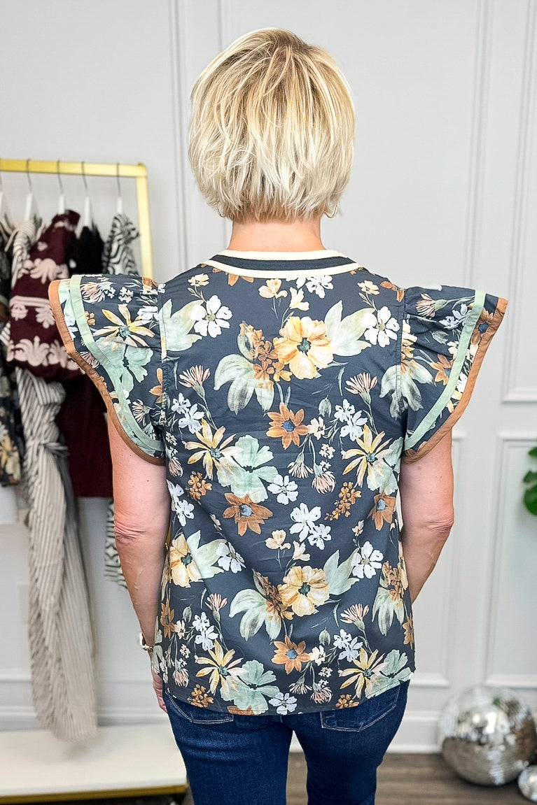 Person wearing a floral blouse with ruffled sleeves in a clothing store.