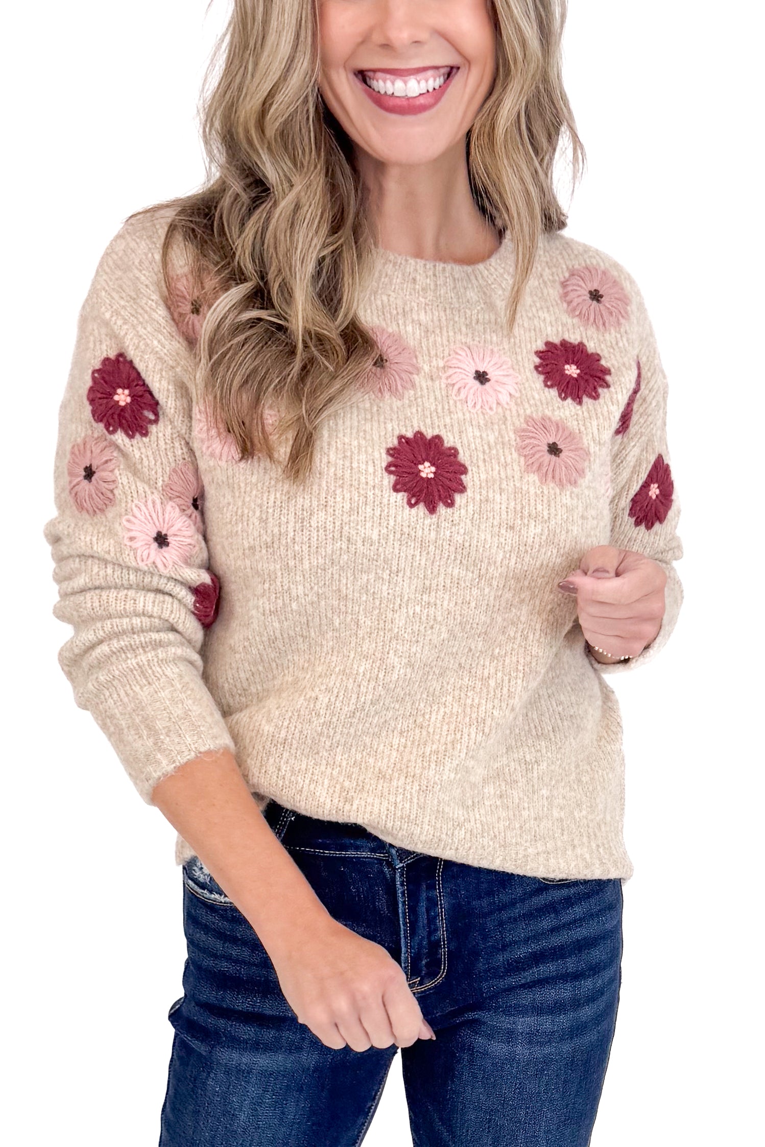 Woman wearing a beige sweater with floral patterns, smiling against a white background