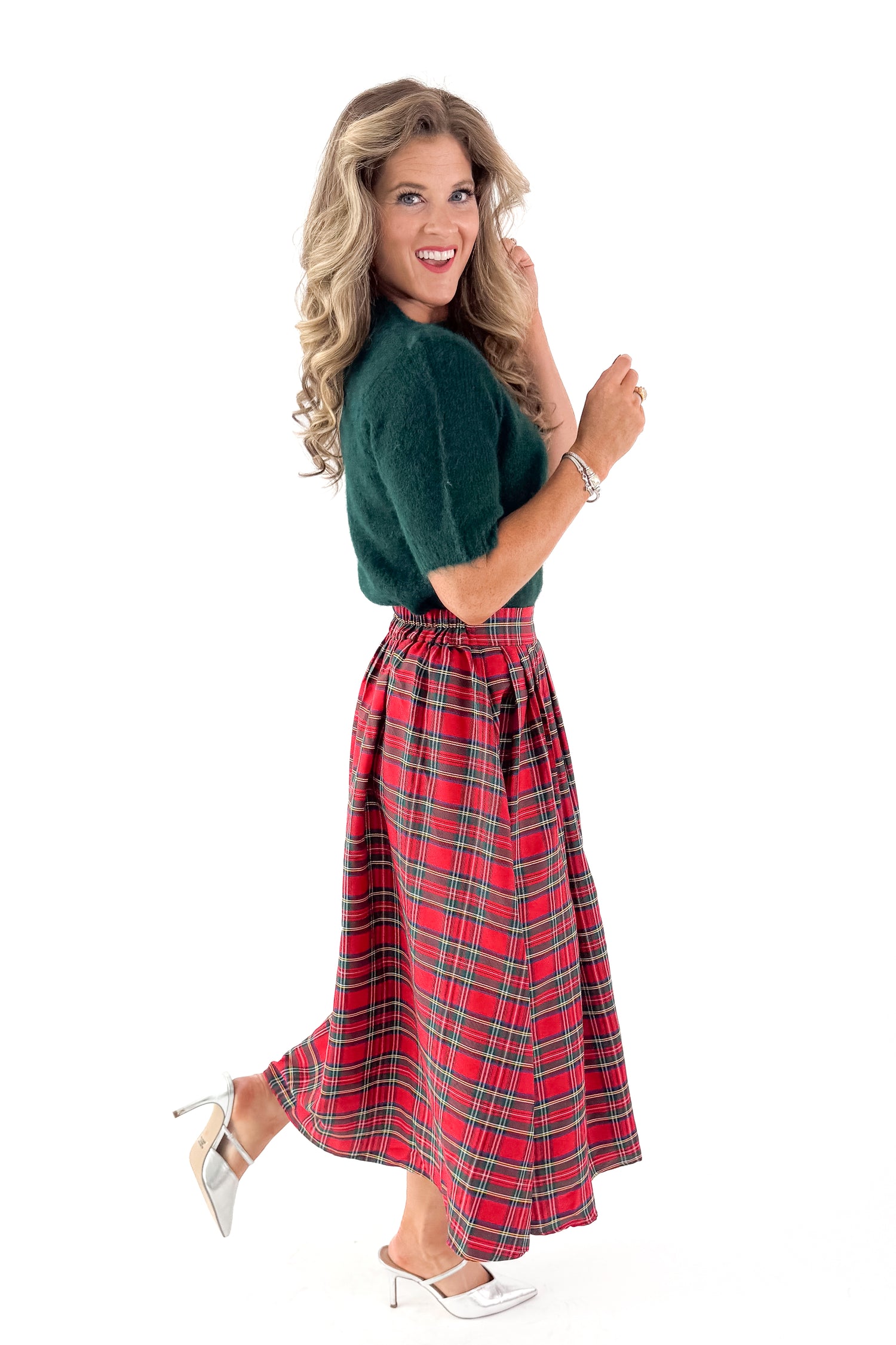 Side view of woman wearing green sweater with red skirt and white studio background.