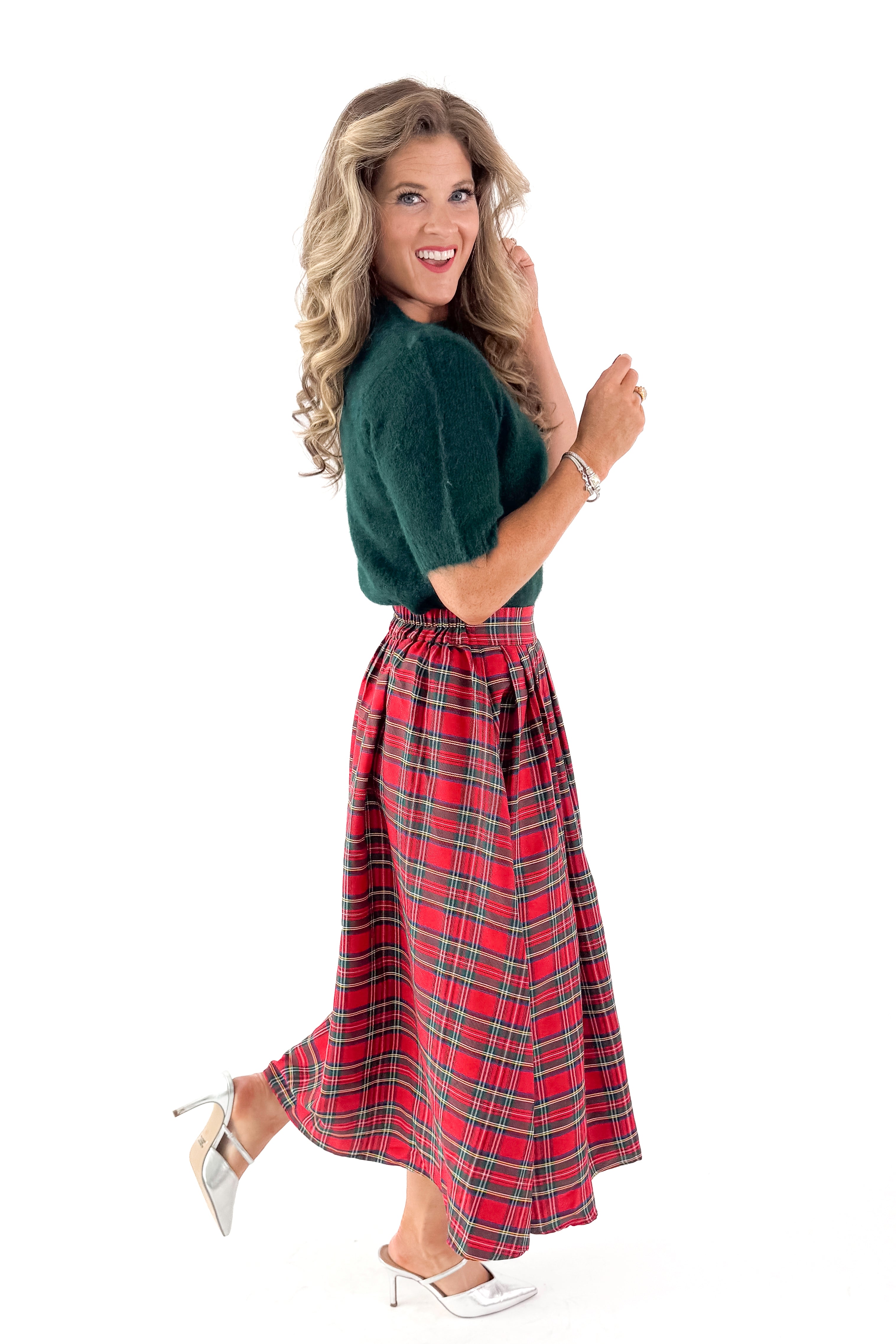 Side view of woman wearing green sweater with red skirt and white studio background.