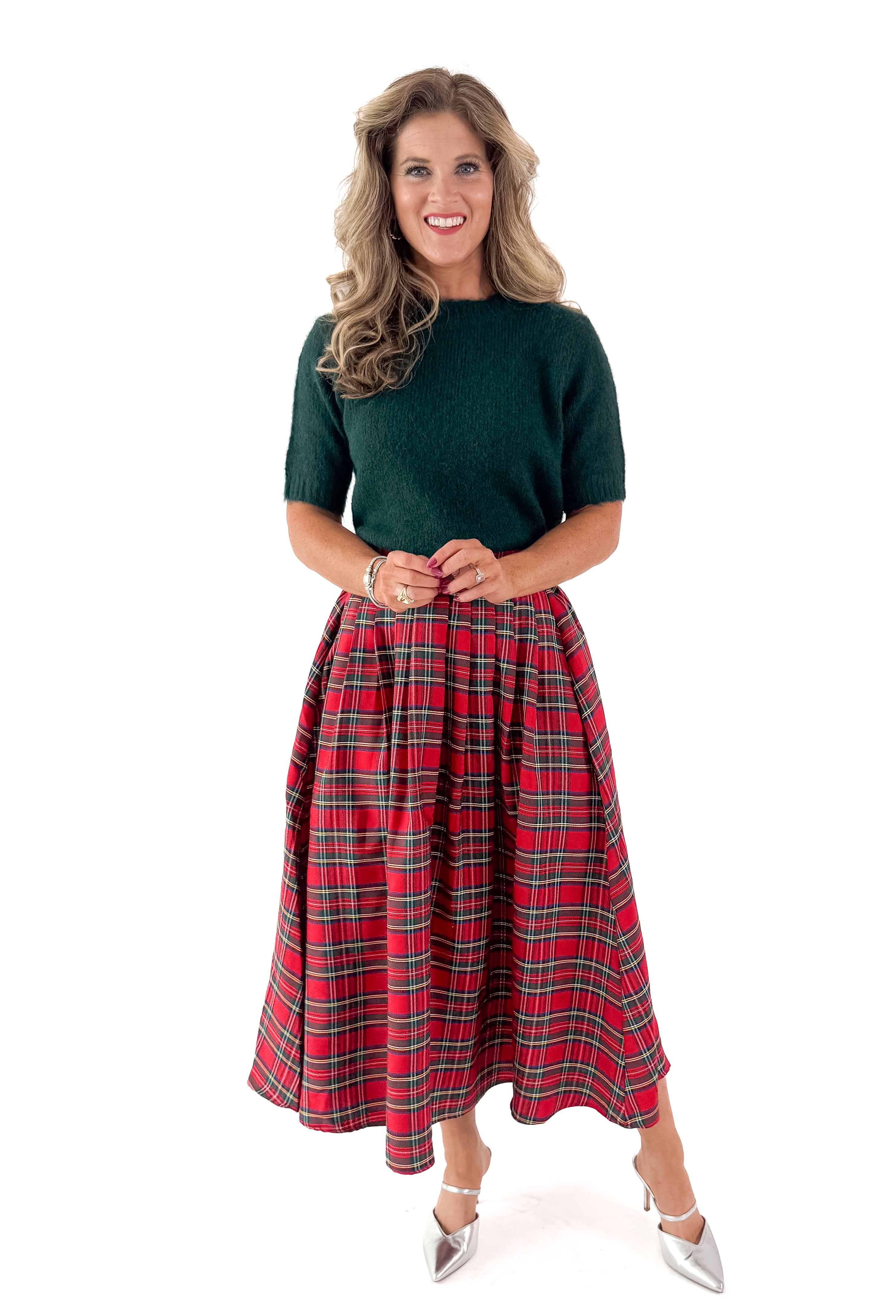 Front view of woman wearing green sweater with red skirt and white studio background.