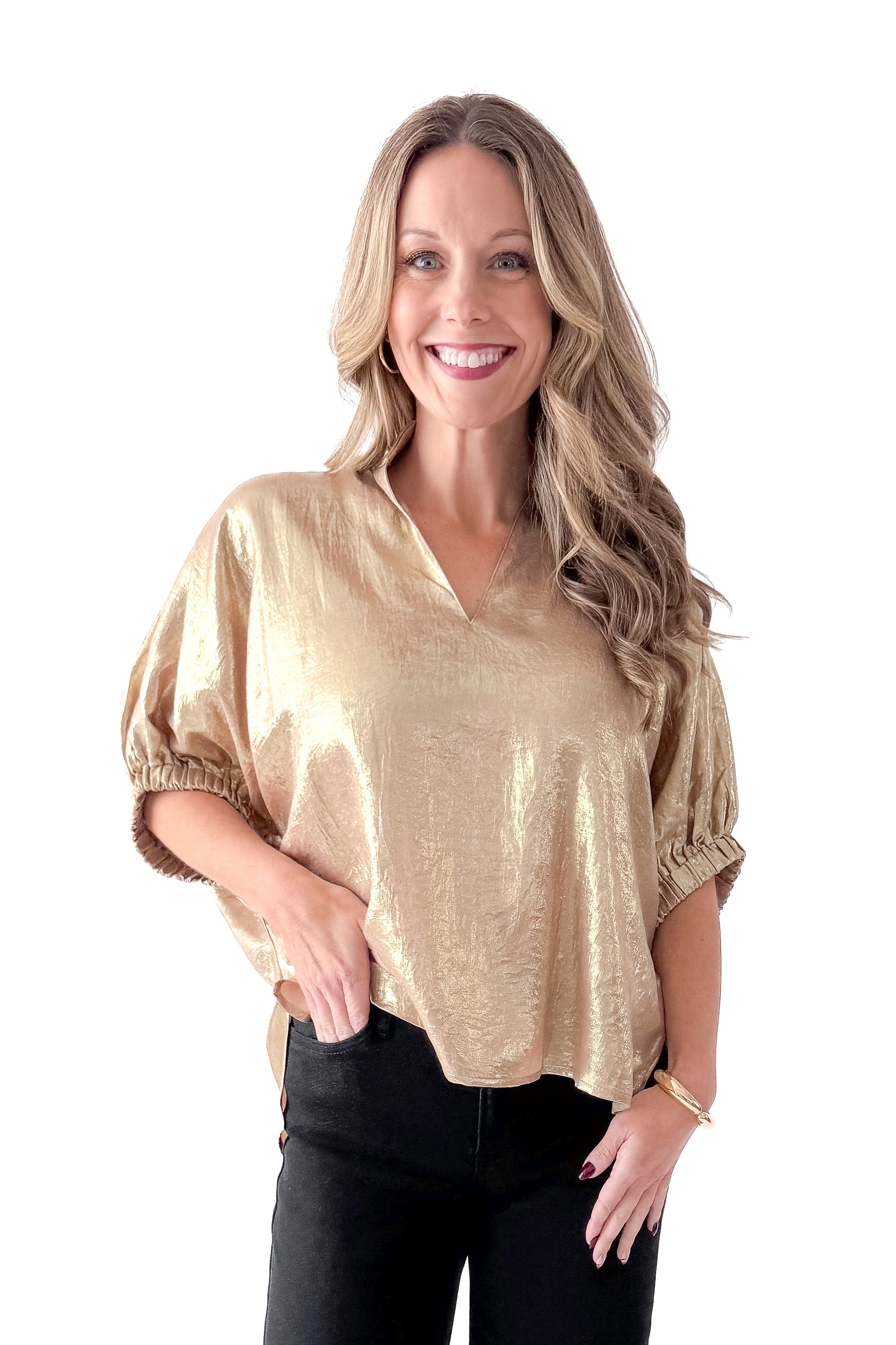 Front view of woman wearing gold metallic top with black jeans against white studio background.