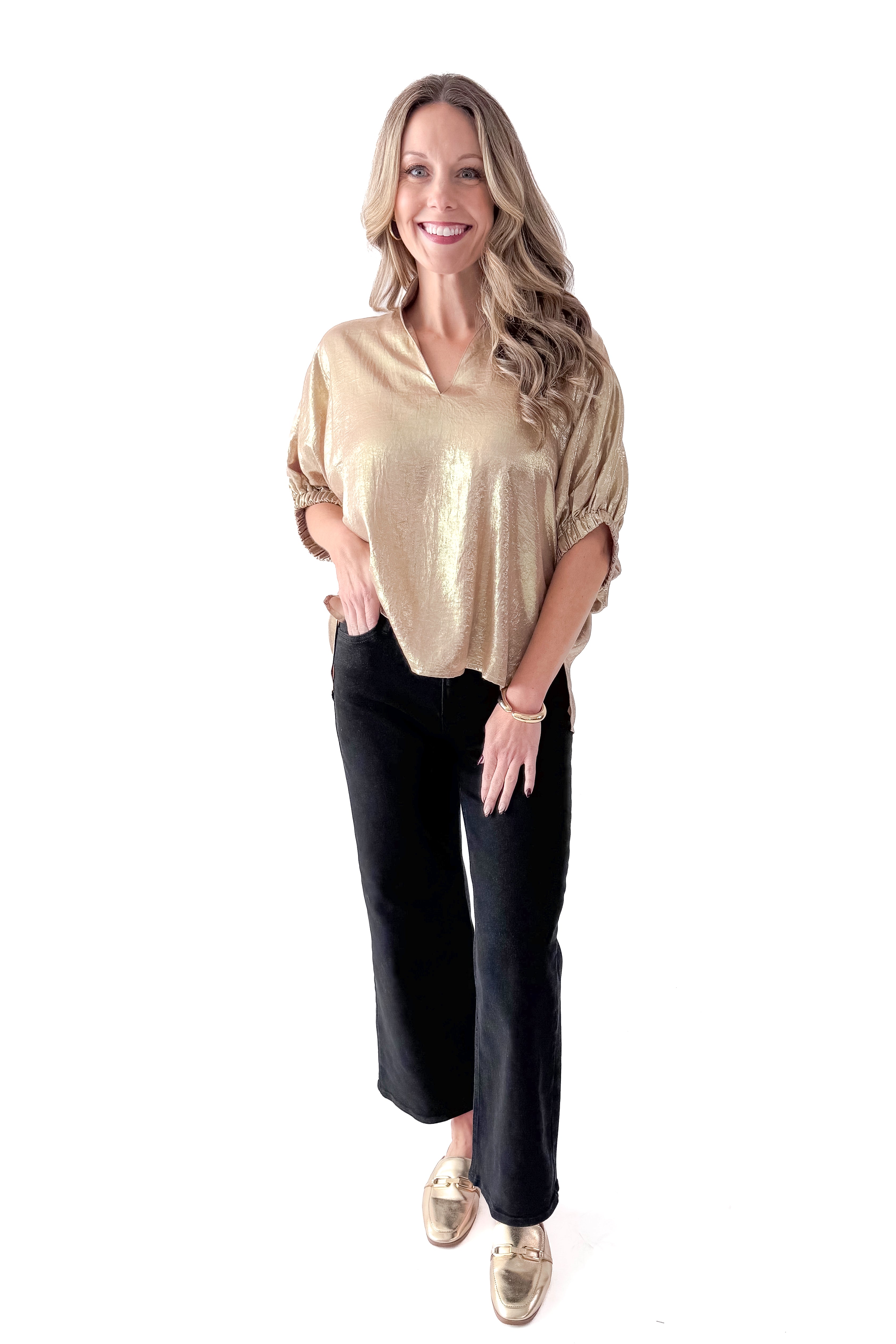 Front view of woman wearing gold metallic top with black jeans against white studio background.