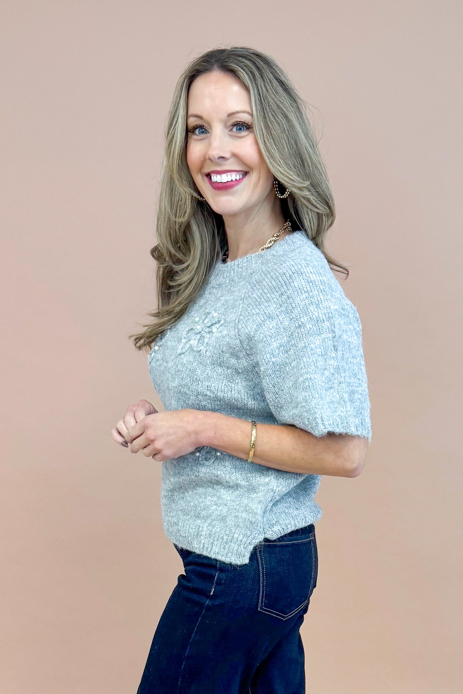 Side view of woman wearing Grey Floral & Pearl Detail Short Sleeve Sweater by Entro and blue jeans.