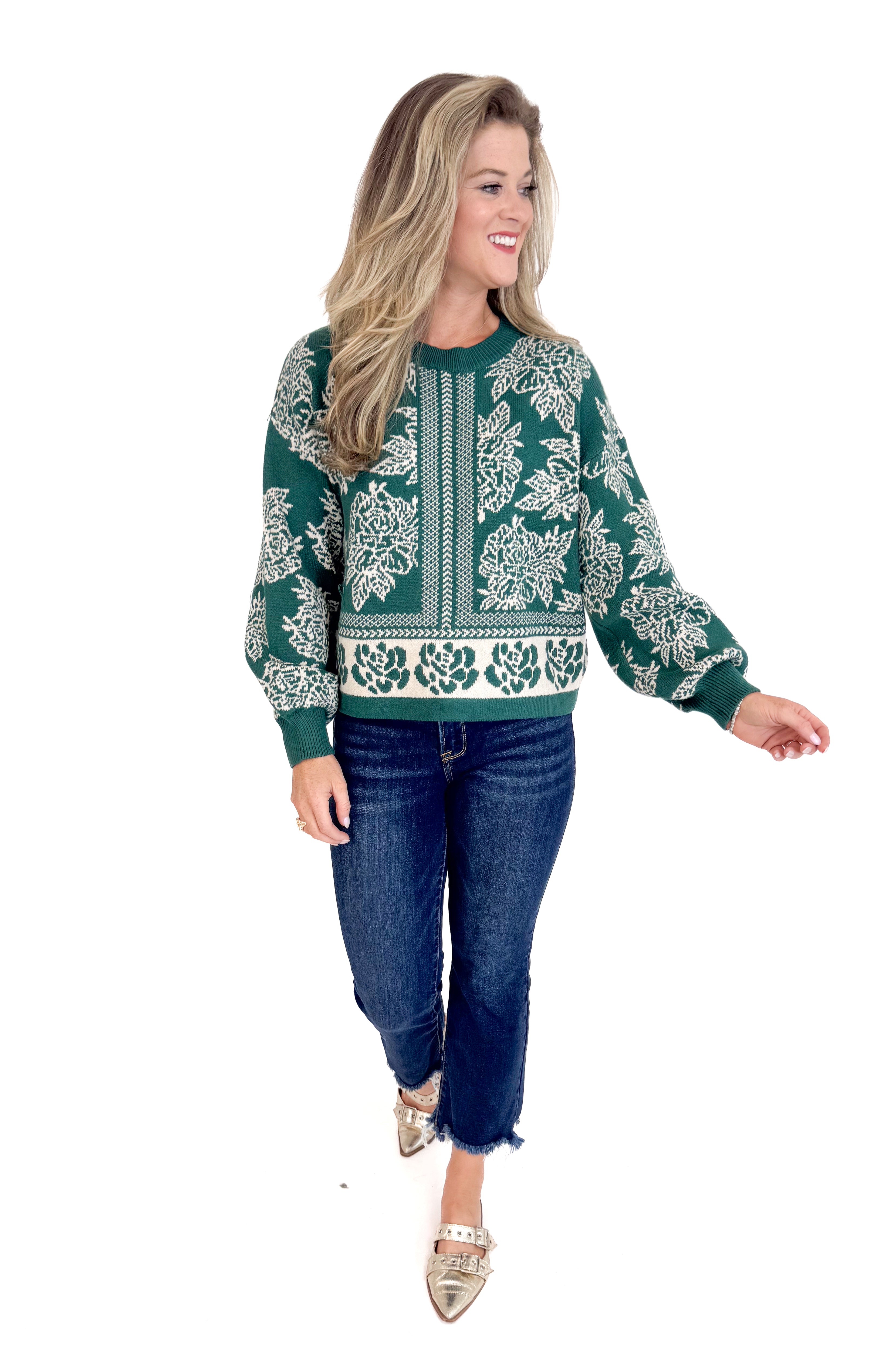 Woman wearing a green patterned sweater and blue jeans on a white background
