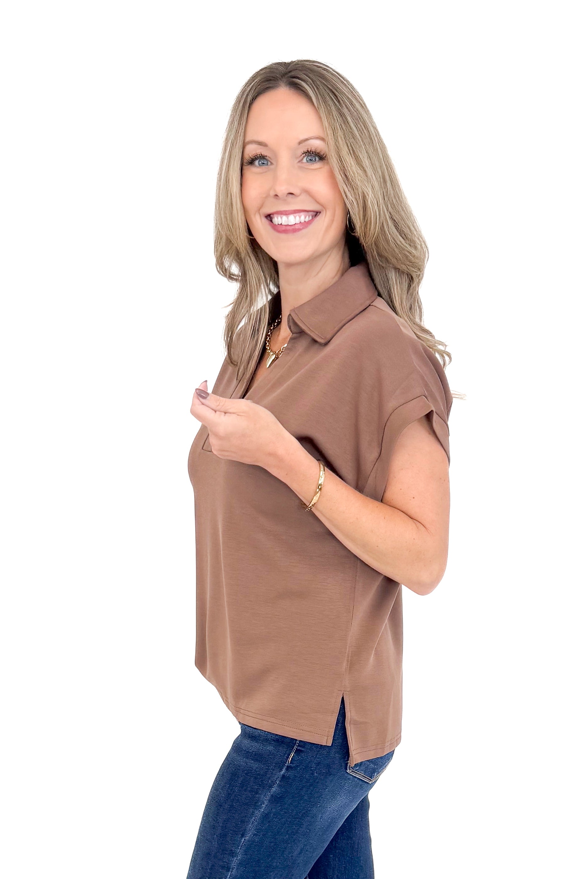 Side view of woman wearing coffee color top with jeans against white studio background.