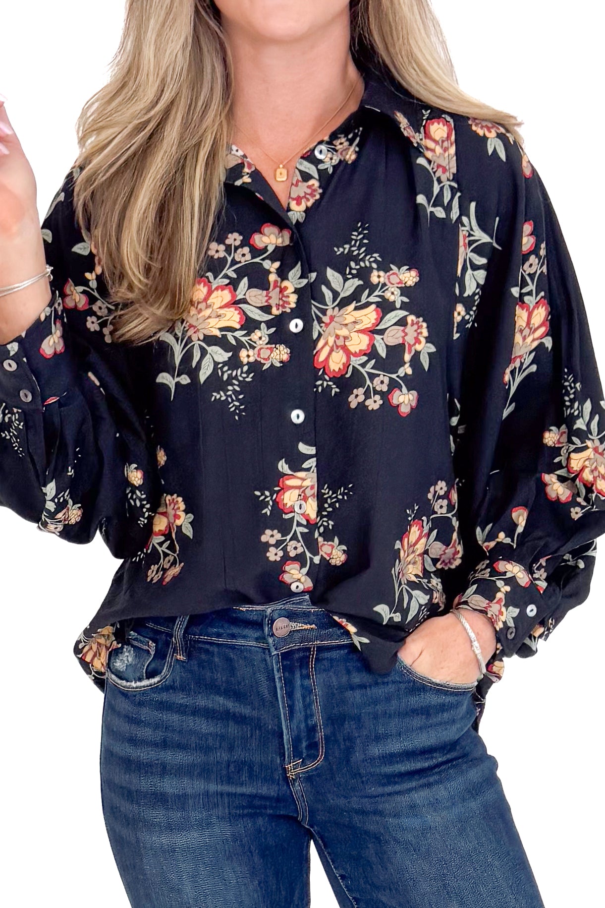 Woman wearing a dark floral blouse and blue jeans on a white background