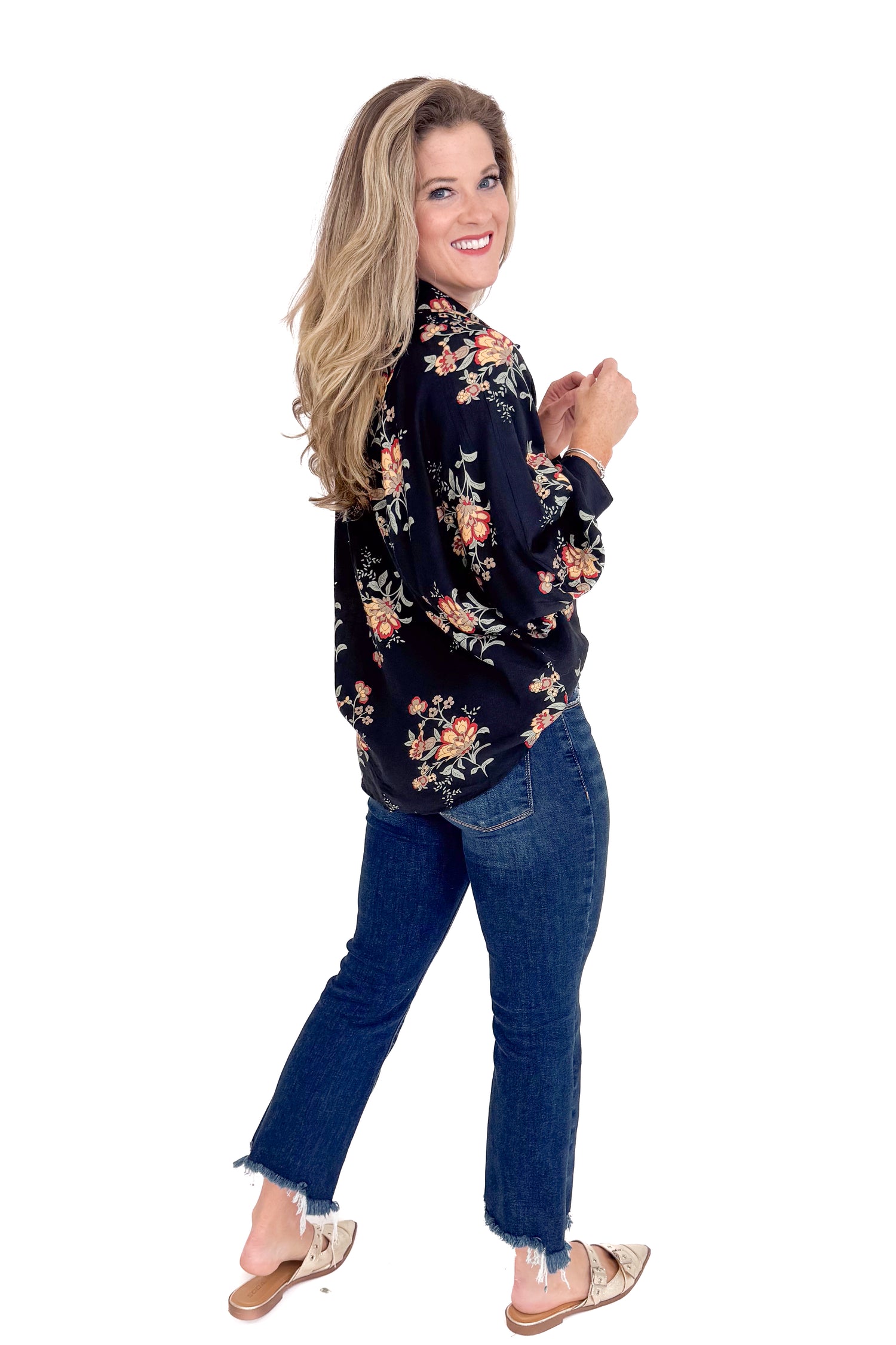 Woman wearing a black floral blouse and blue jeans on a white background