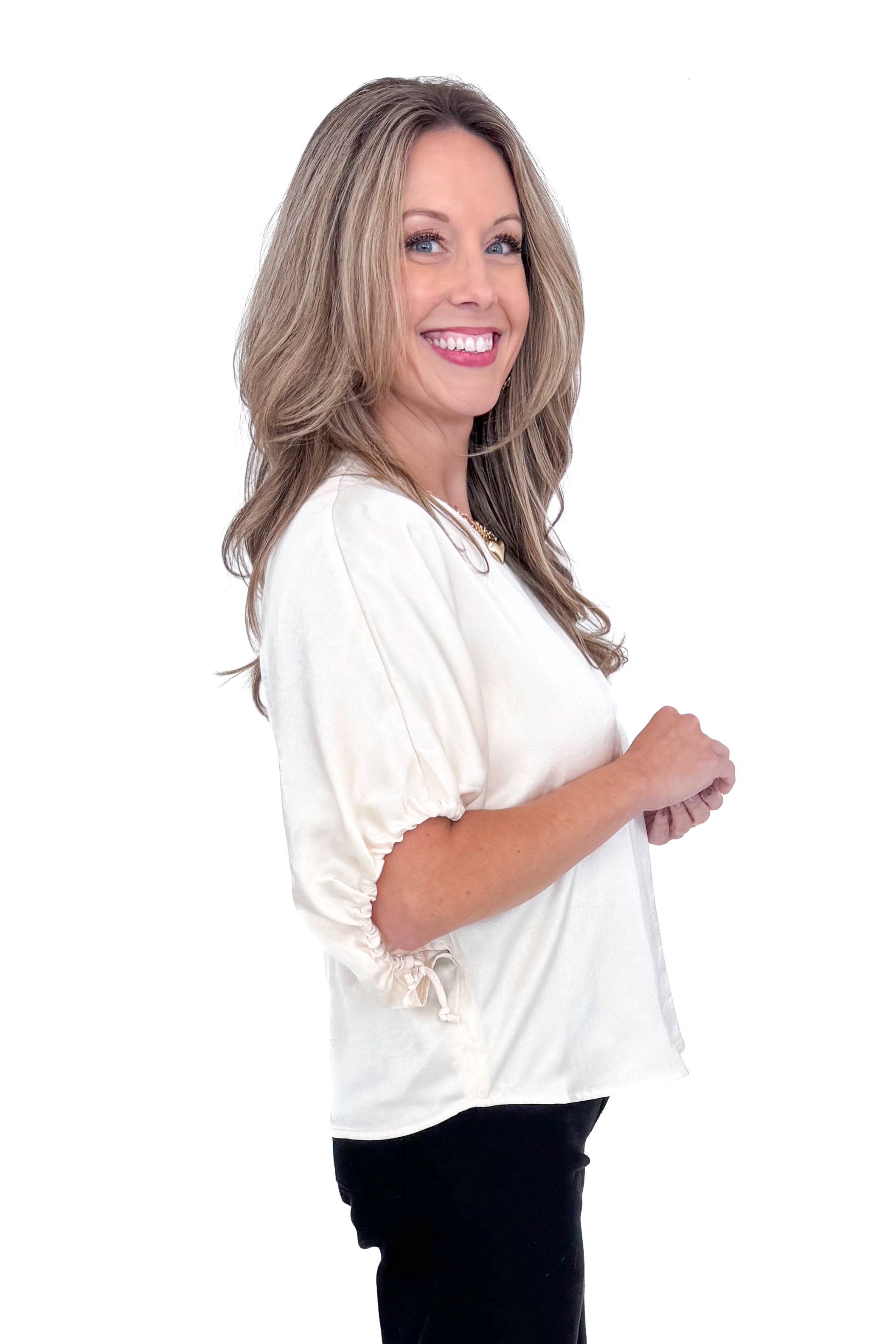 Side view of woman wearing Champagne Satin Tie Sleeve Top with jeans against white studio background.