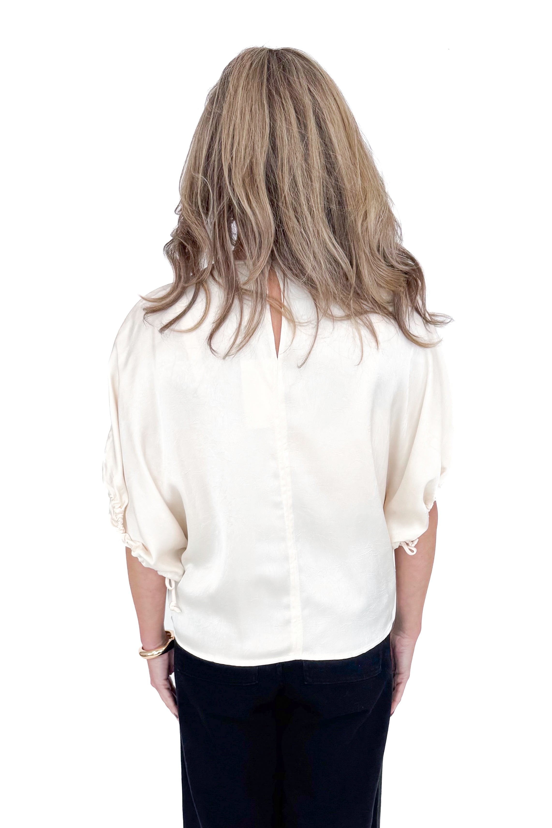 Back view of woman wearing Champagne Satin Tie Sleeve Top with jeans against white studio background.