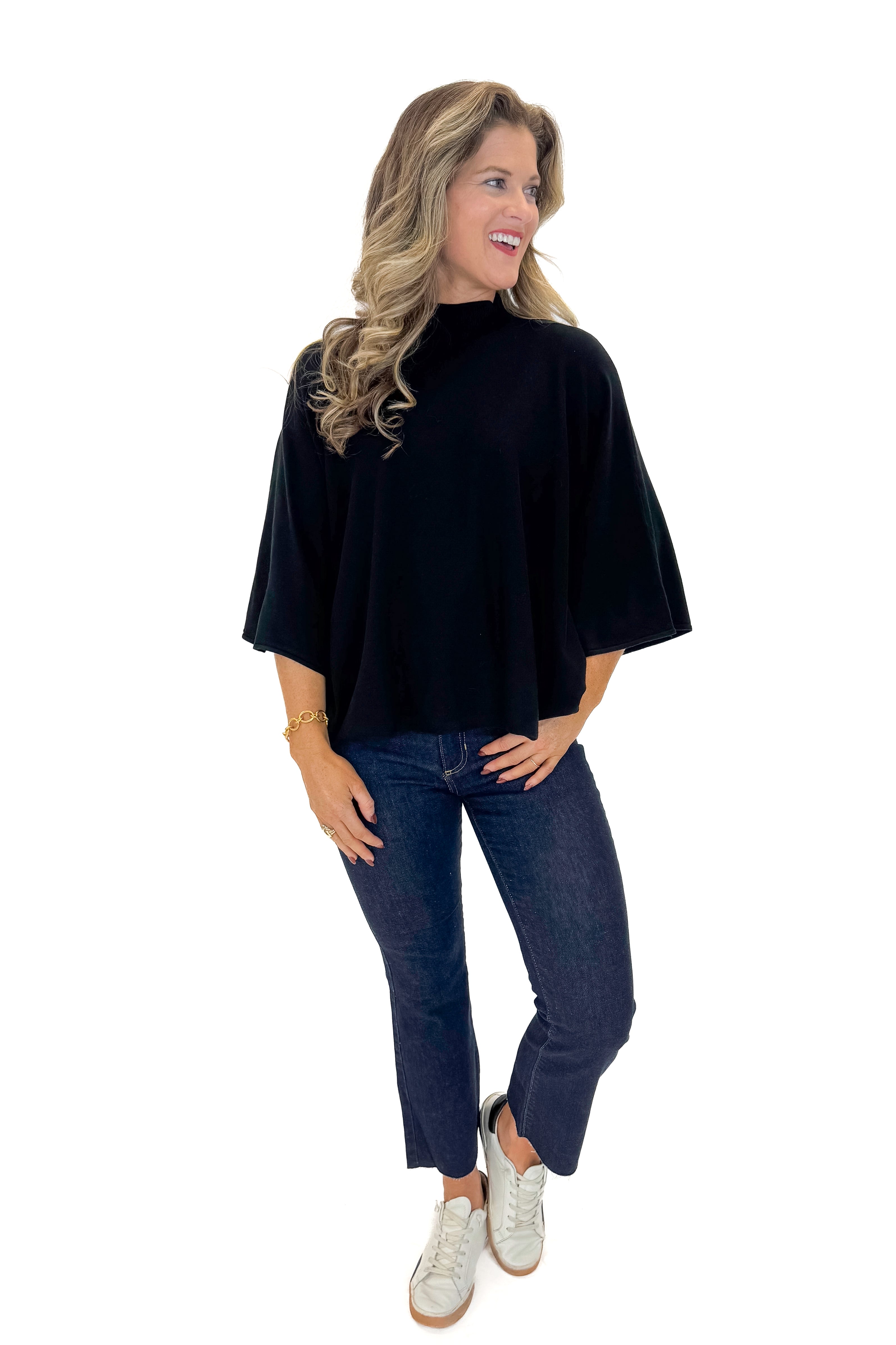 Front view of woman wearing Black Mock Neck Poncho Sweater with jeans against white studio background.