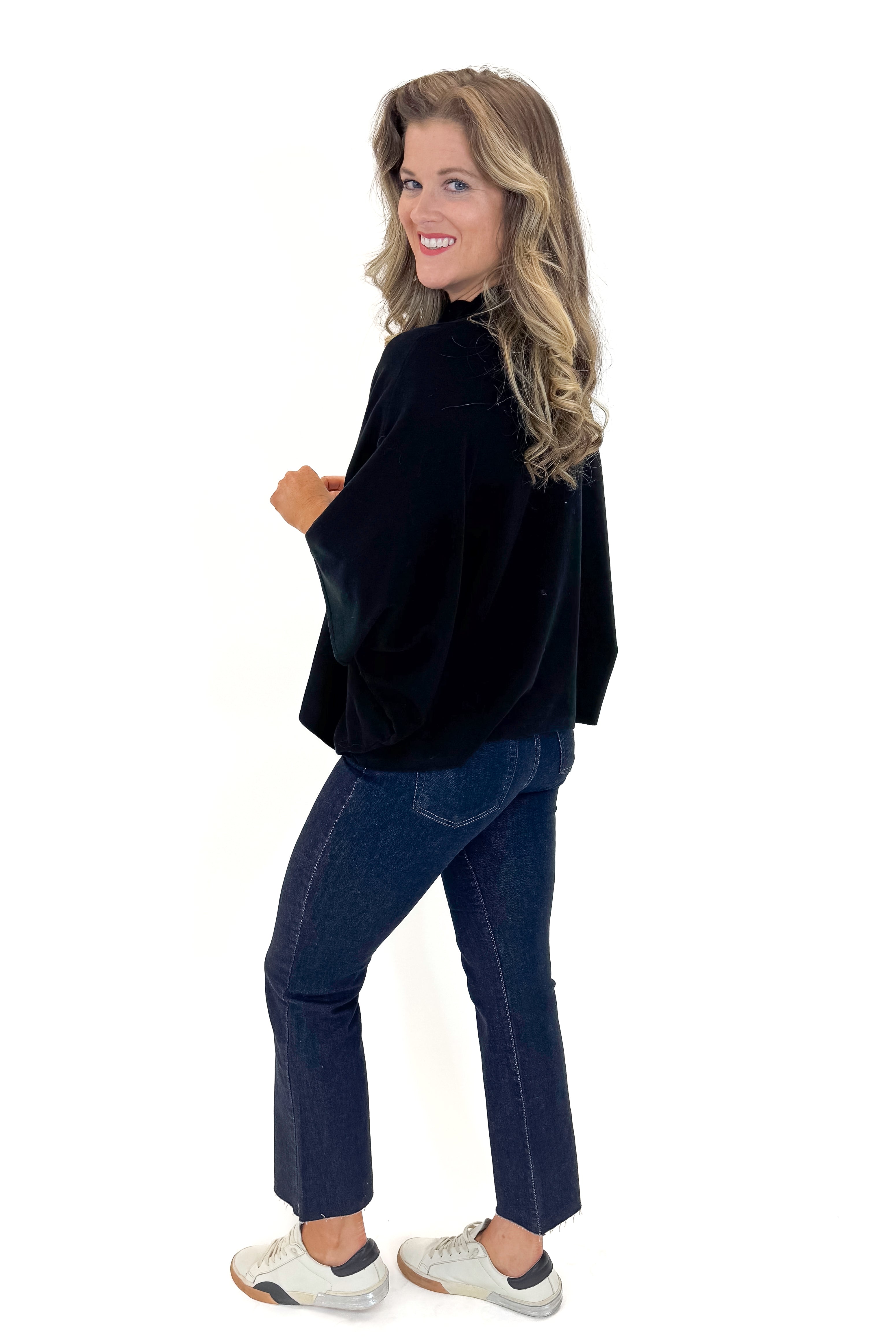 Side view of woman wearing Black Mock Neck Poncho Sweater with jeans against white studio background.