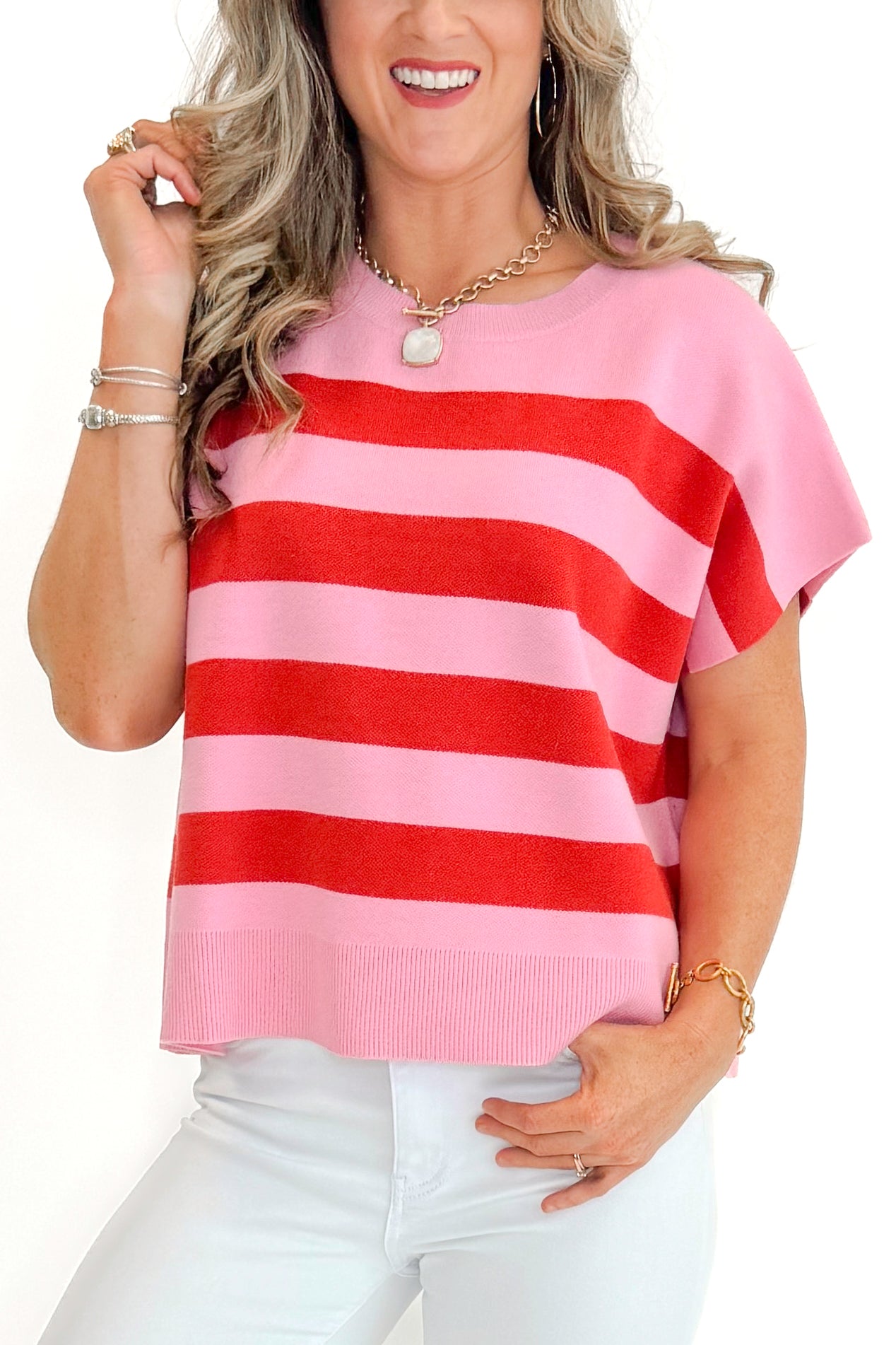 Front detail view of woman wearing Pink & Red Sleeveless Sweater by Entro with jeans against white studio background.
