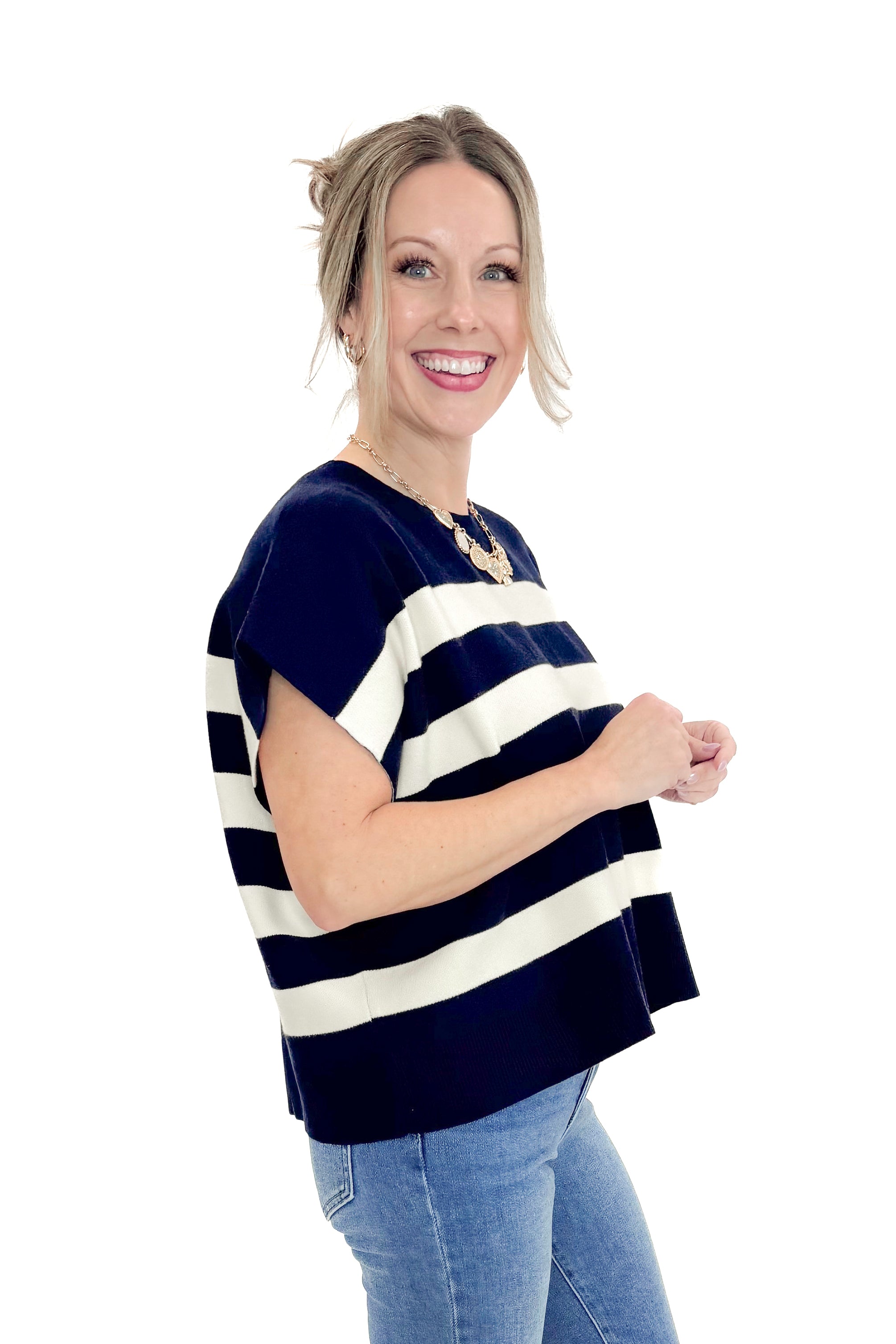 Side view of woman wearing Navy & Cream Sleeveless Sweater by Entro with jeans against white studio background.