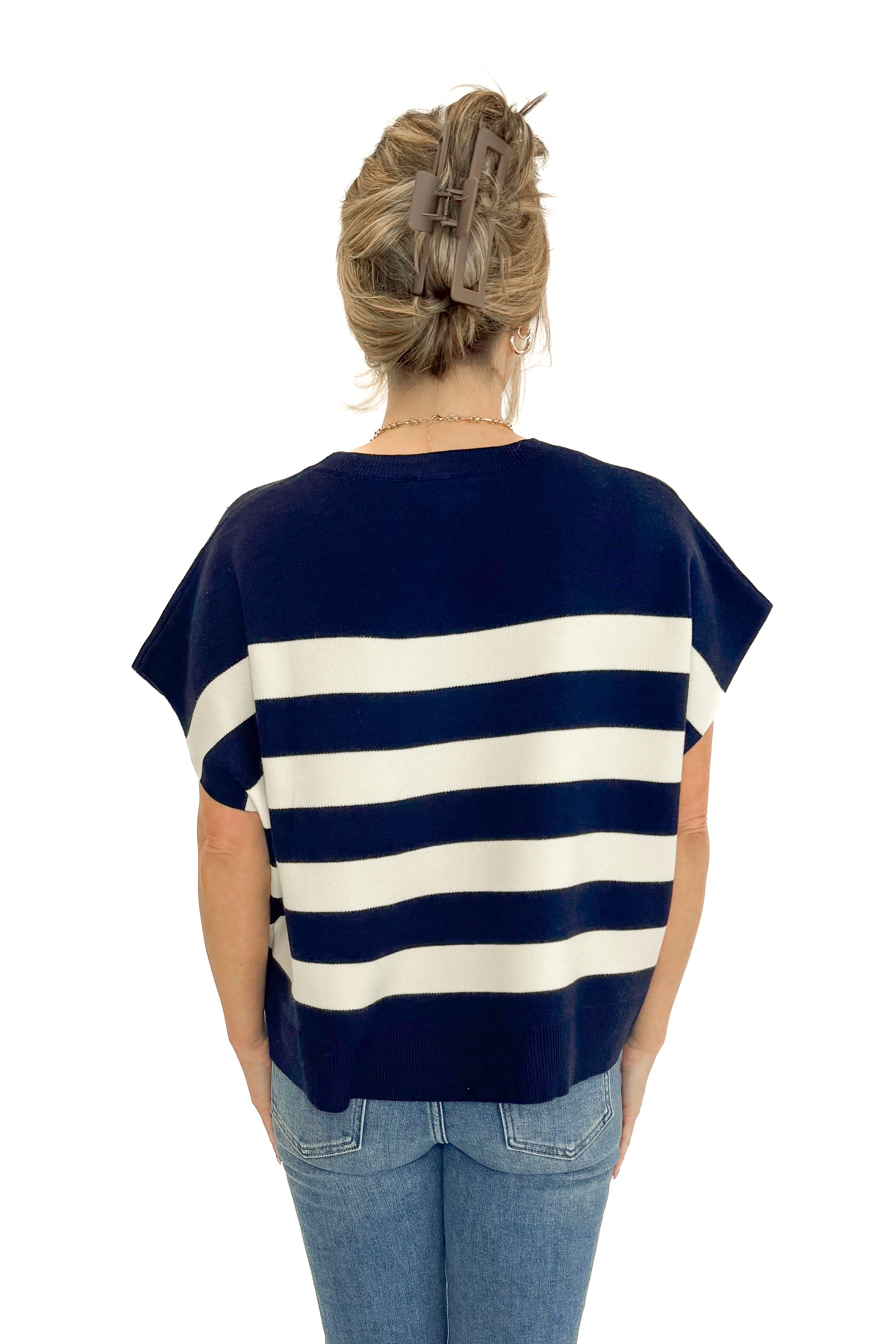 Back view of woman wearing Navy & Cream Sleeveless Sweater by Entro with jeans against white studio background.
