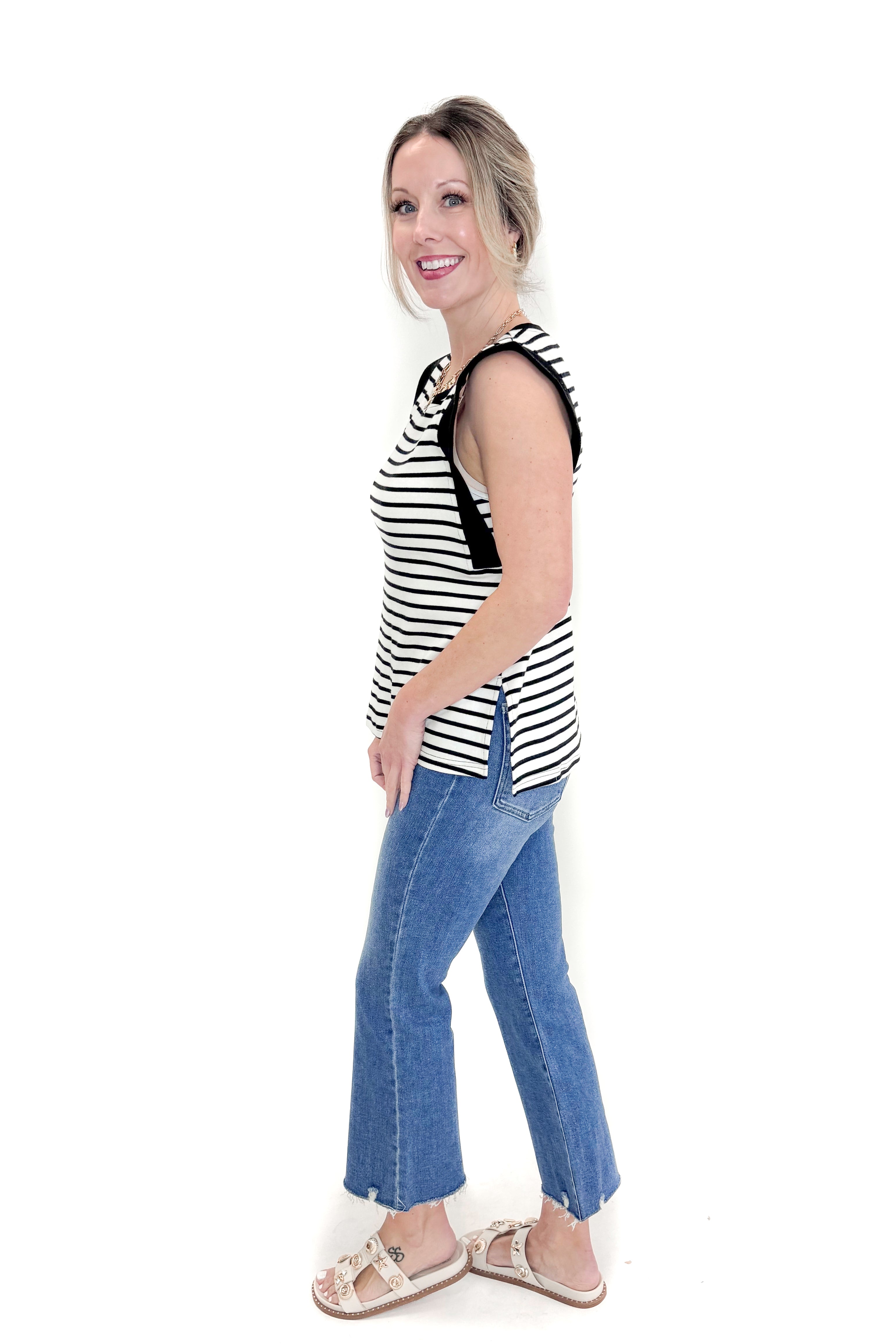 Side view of woman wearing White & Black Striped Sleeveless Top by Entro with jeans against white studio background.