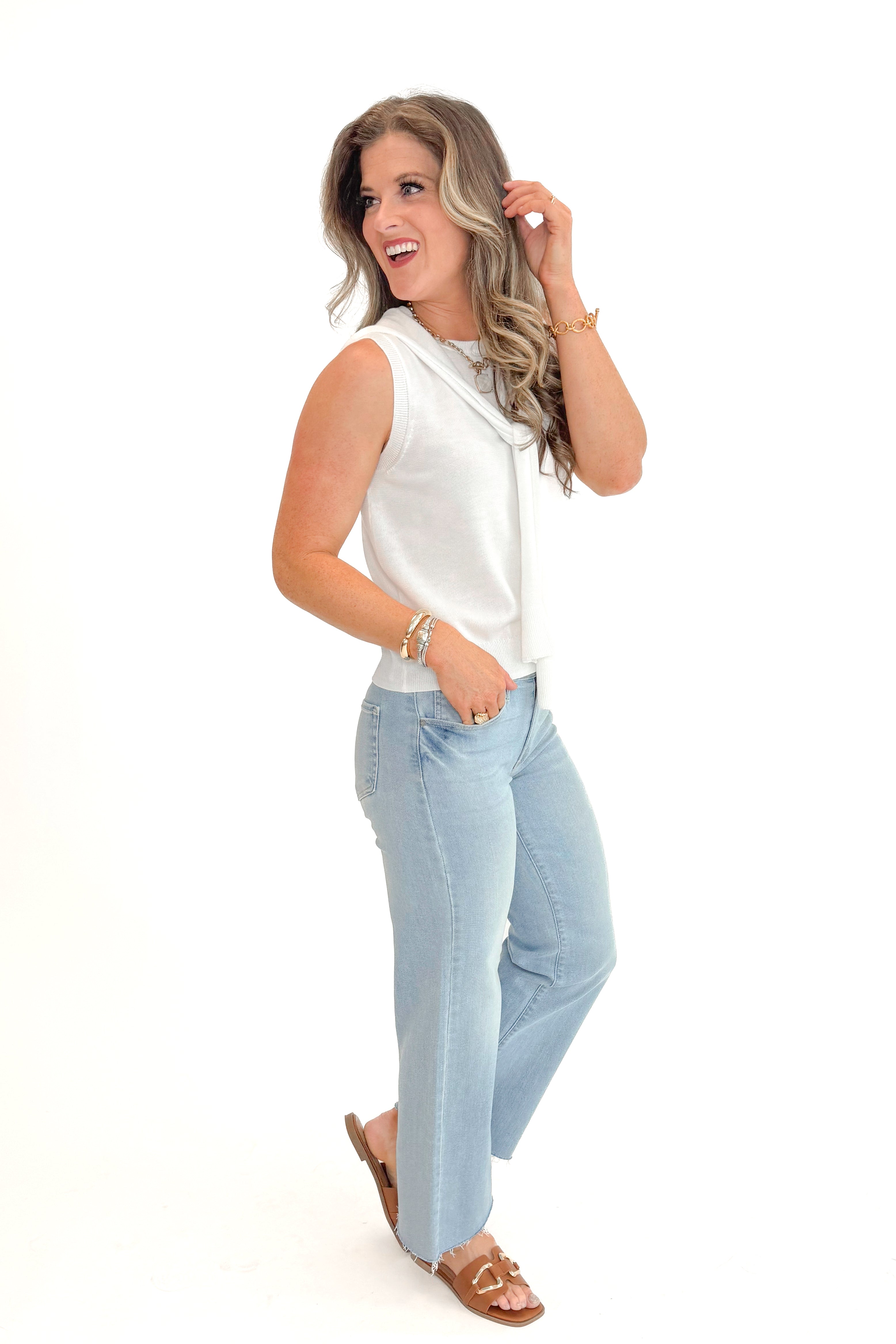 Side view of woman wearing Ivory Faux Layered Sweater Tank by Entro with jeans against white studio background.