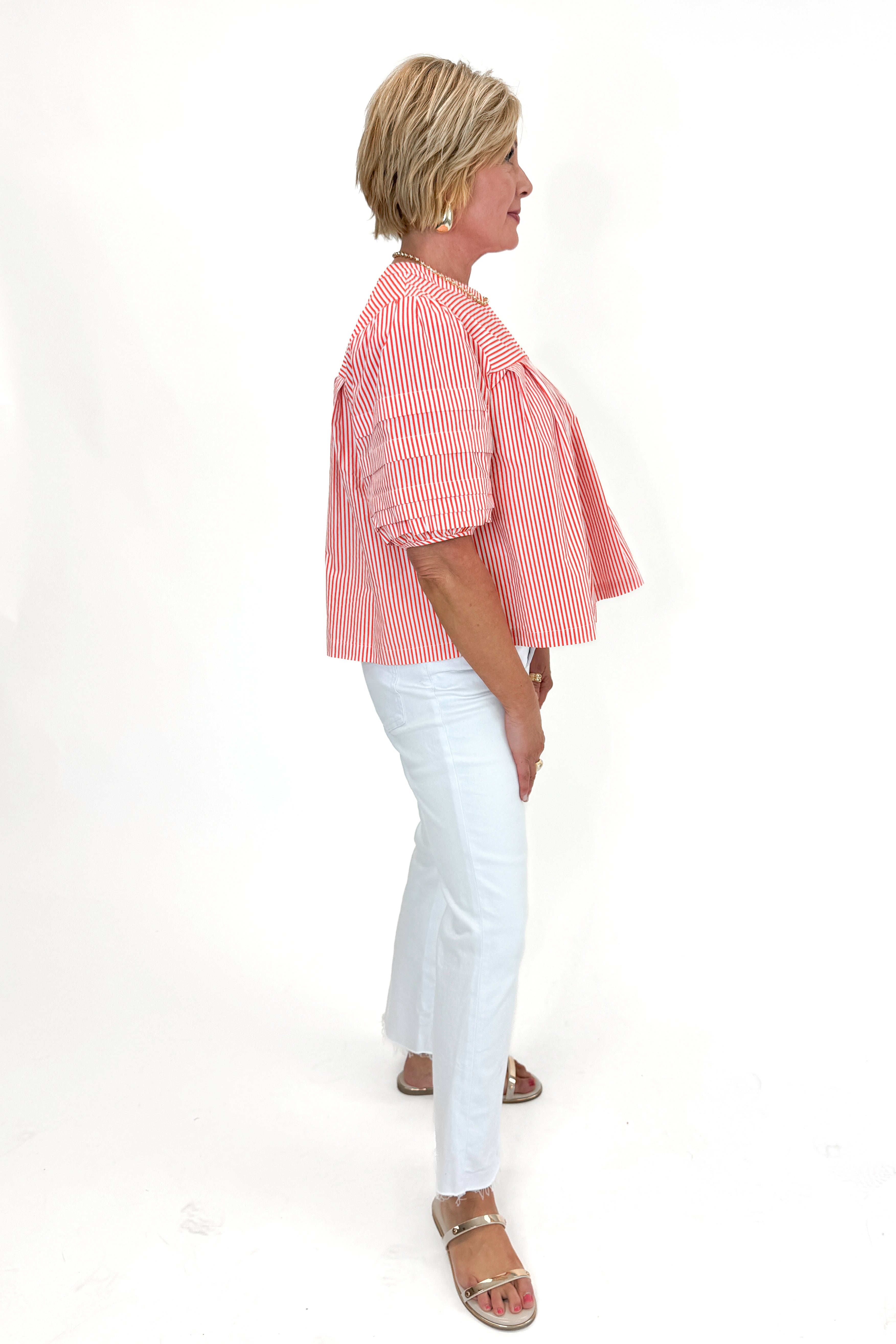 Side view of woman wearing Orange Striped Puff Sleeve Top by Entro with jeans against white studio background.