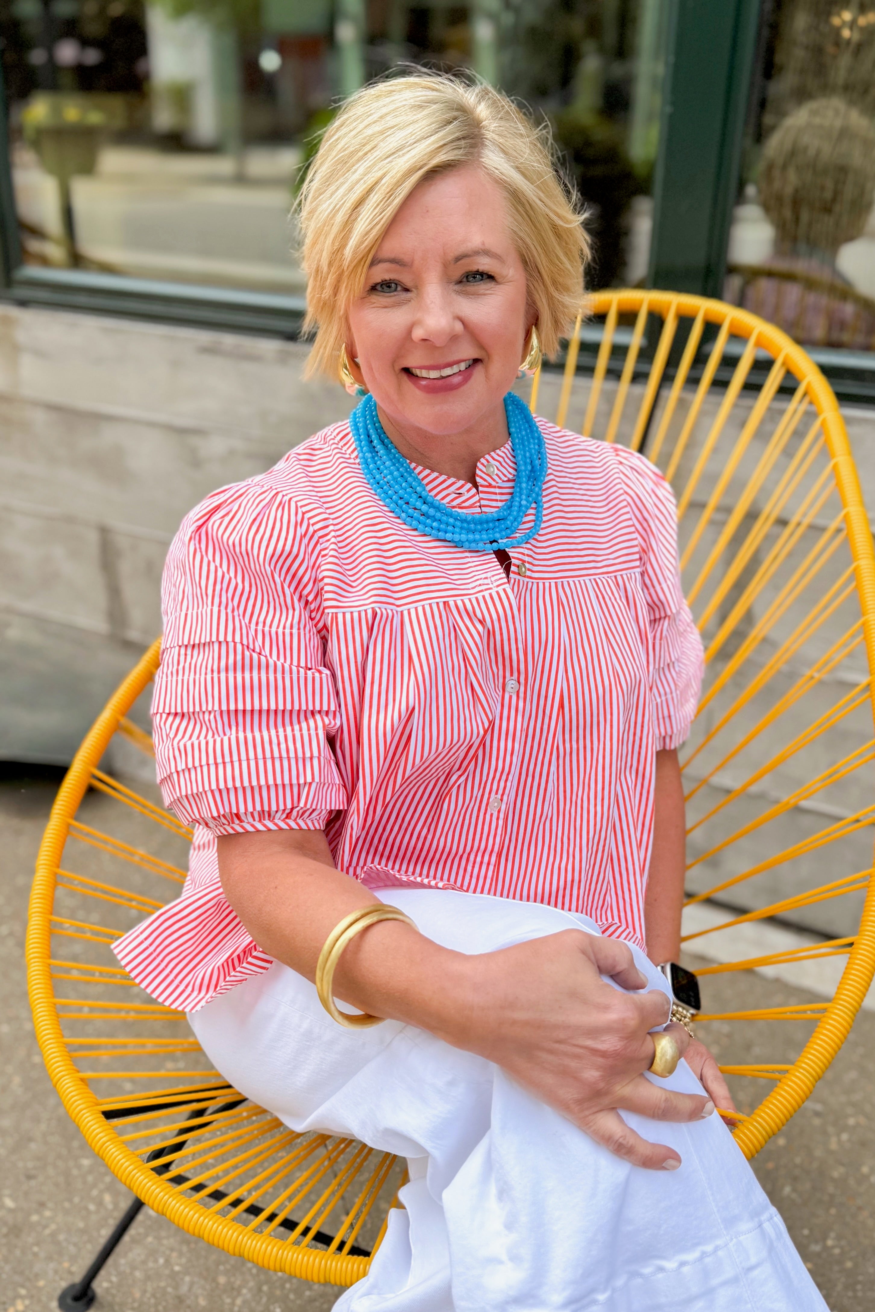 Front view of woman wearing Orange Striped Puff Sleeve Top by Entro with jeans sitting outside.