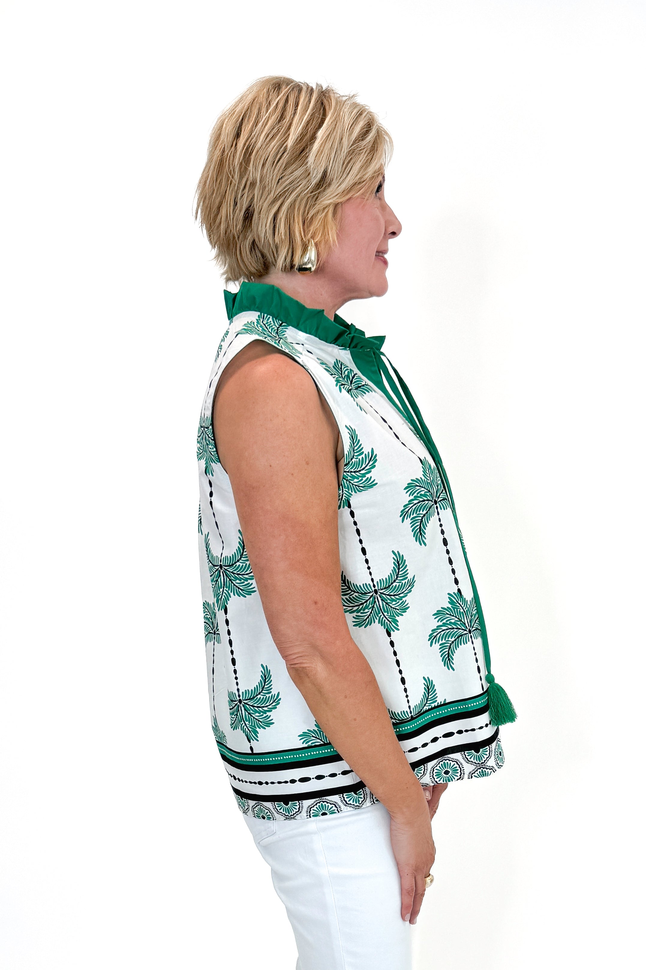 Side view of woman wearing Green Palm Printed Sleeveless Top by Entro with jeans against white studio background.
